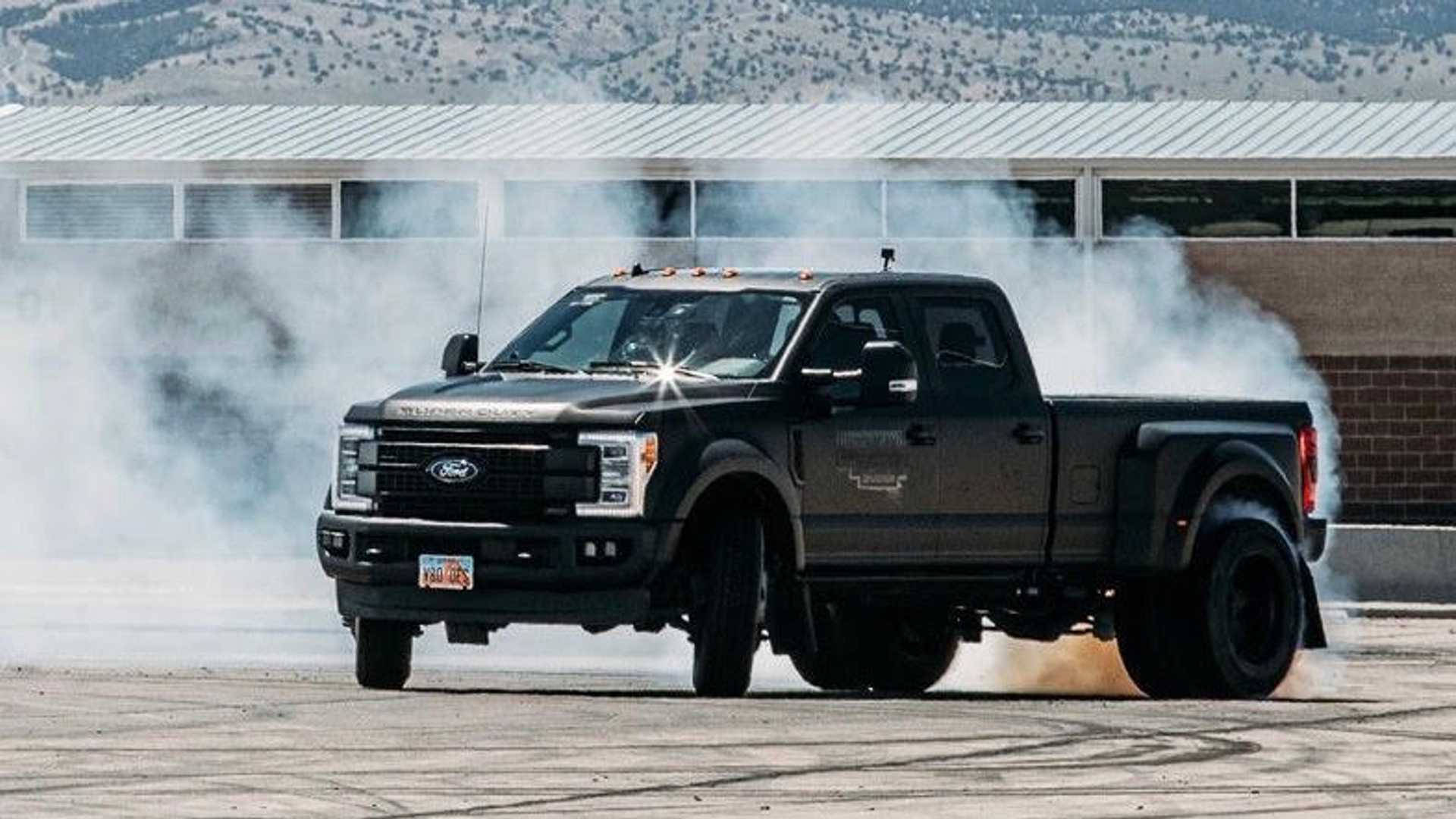 A Black Truck Is Driving Down A Track With Smoke Coming Out Of It Wallpaper