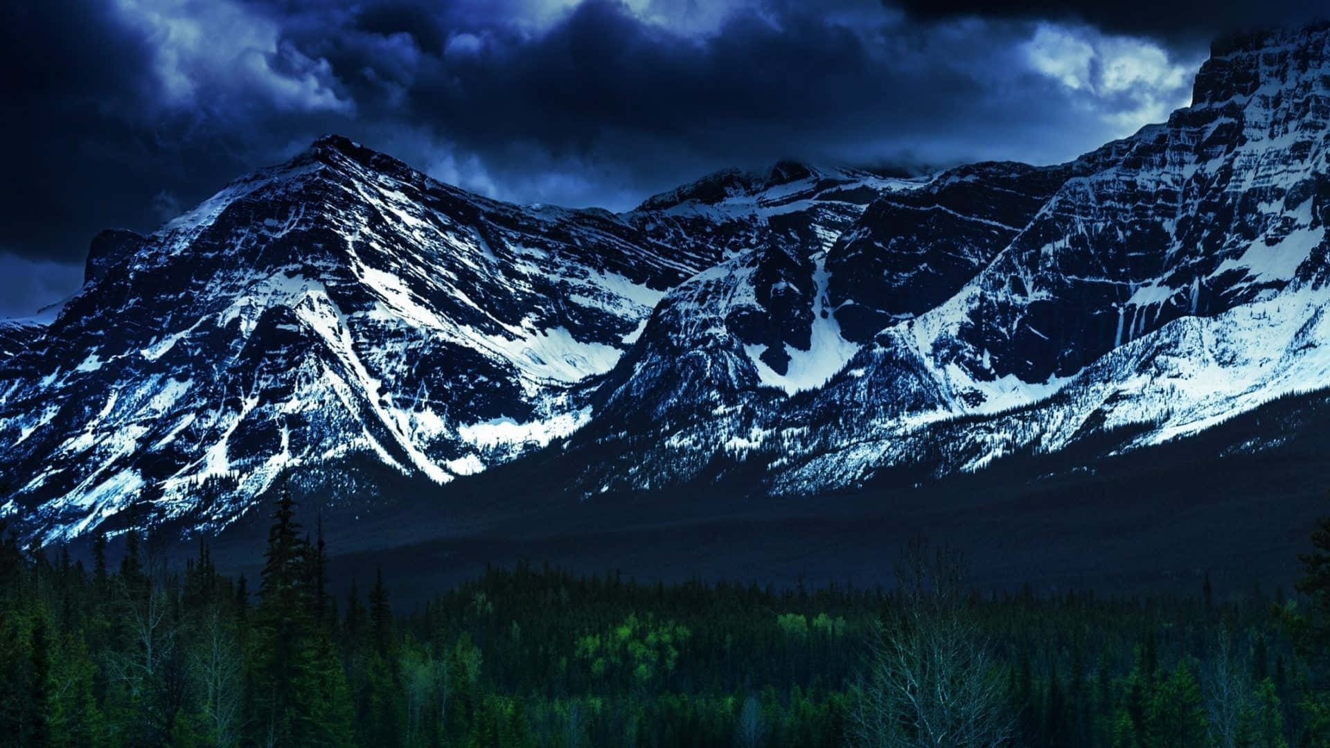 A Mountain Range With Trees And A Dark Sky