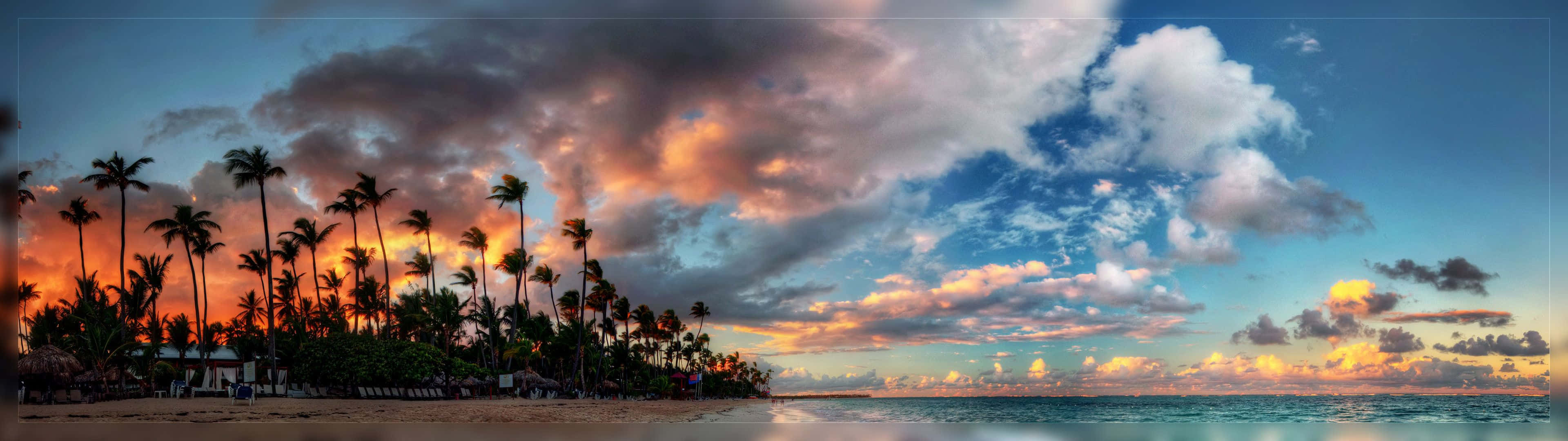 A Sunset With Palm Trees And Clouds On The Beach