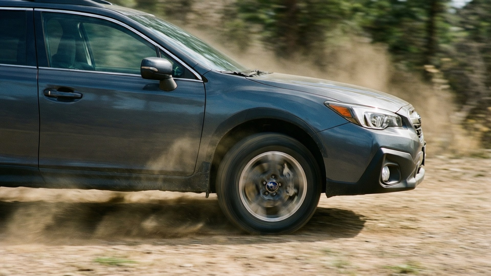 Subaru Outback sideprofil i bevegelse med støv og hastighetsskumring.