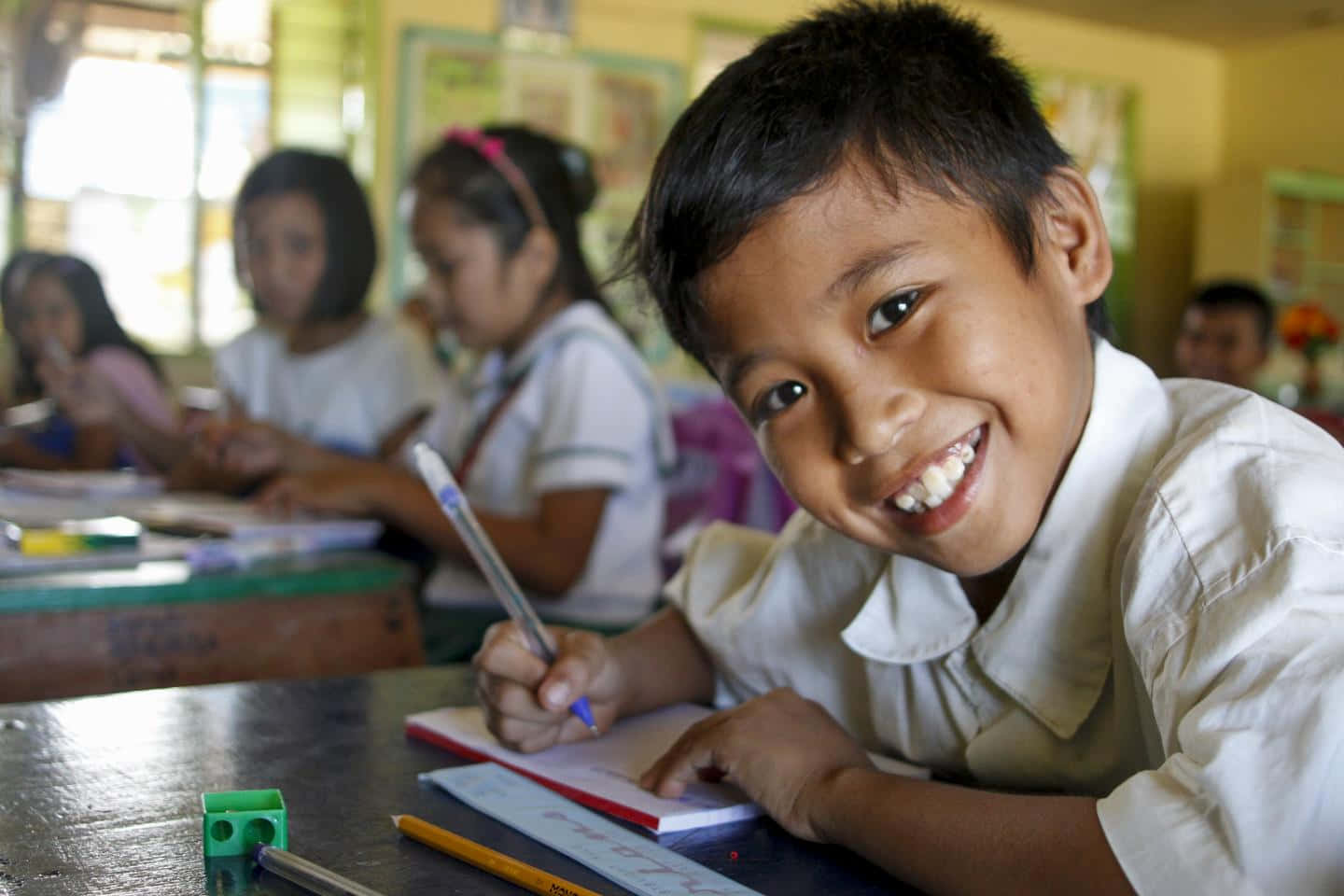 A Boy Smiles While Writing In A Notebook