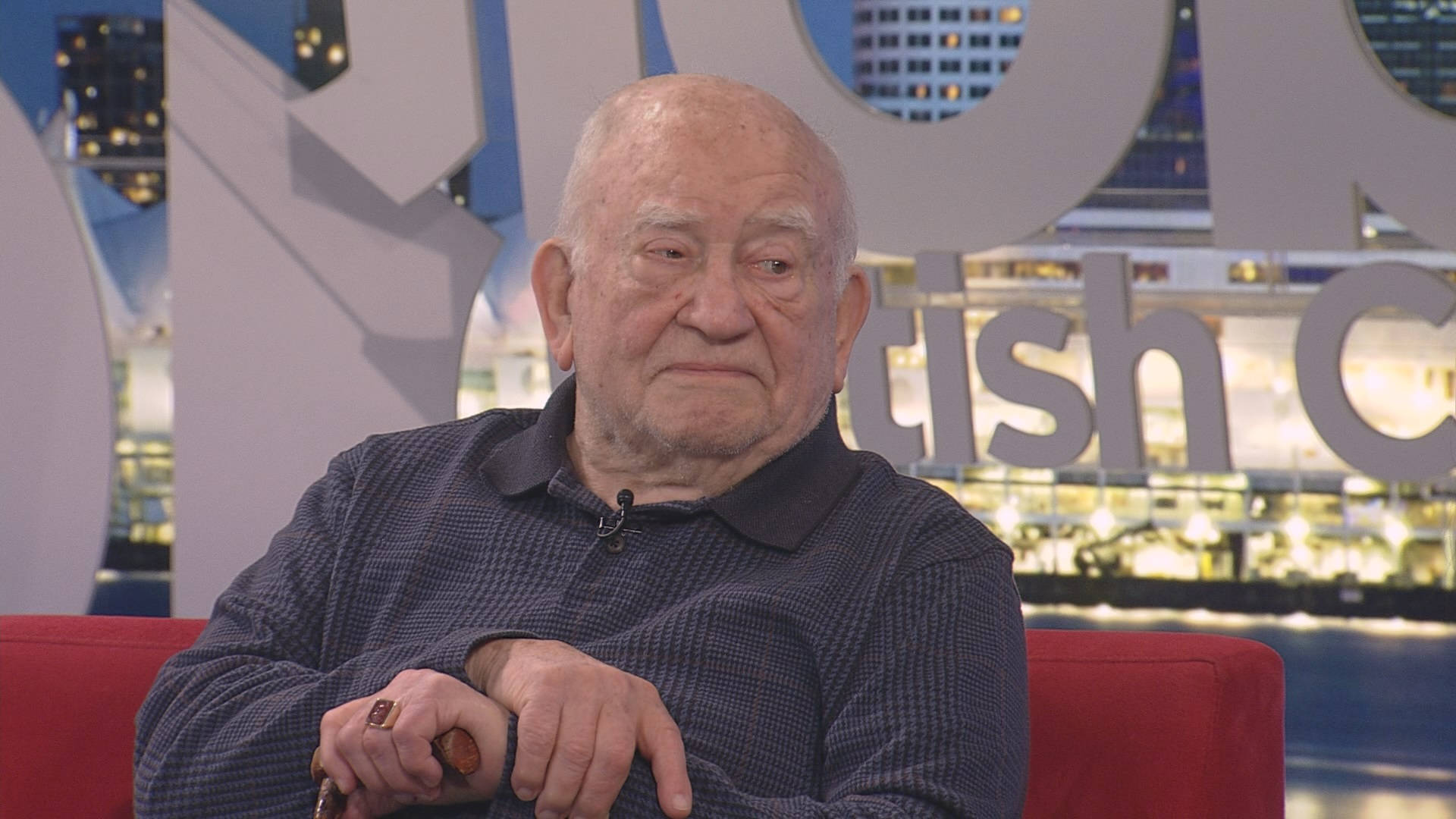 Legendary Actor Edward Asner Relaxing on a Red Couch Wallpaper
