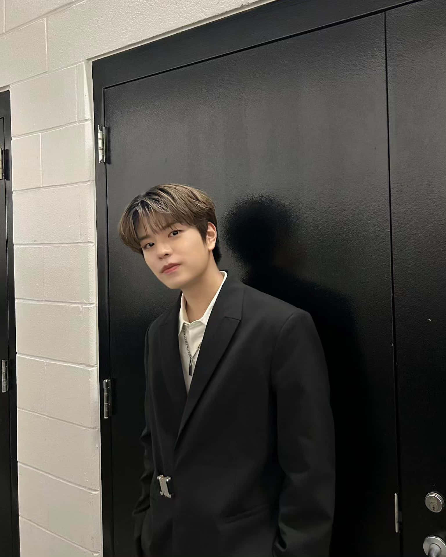 Elegant Young Manin Black Suit Standingby Door Wallpaper