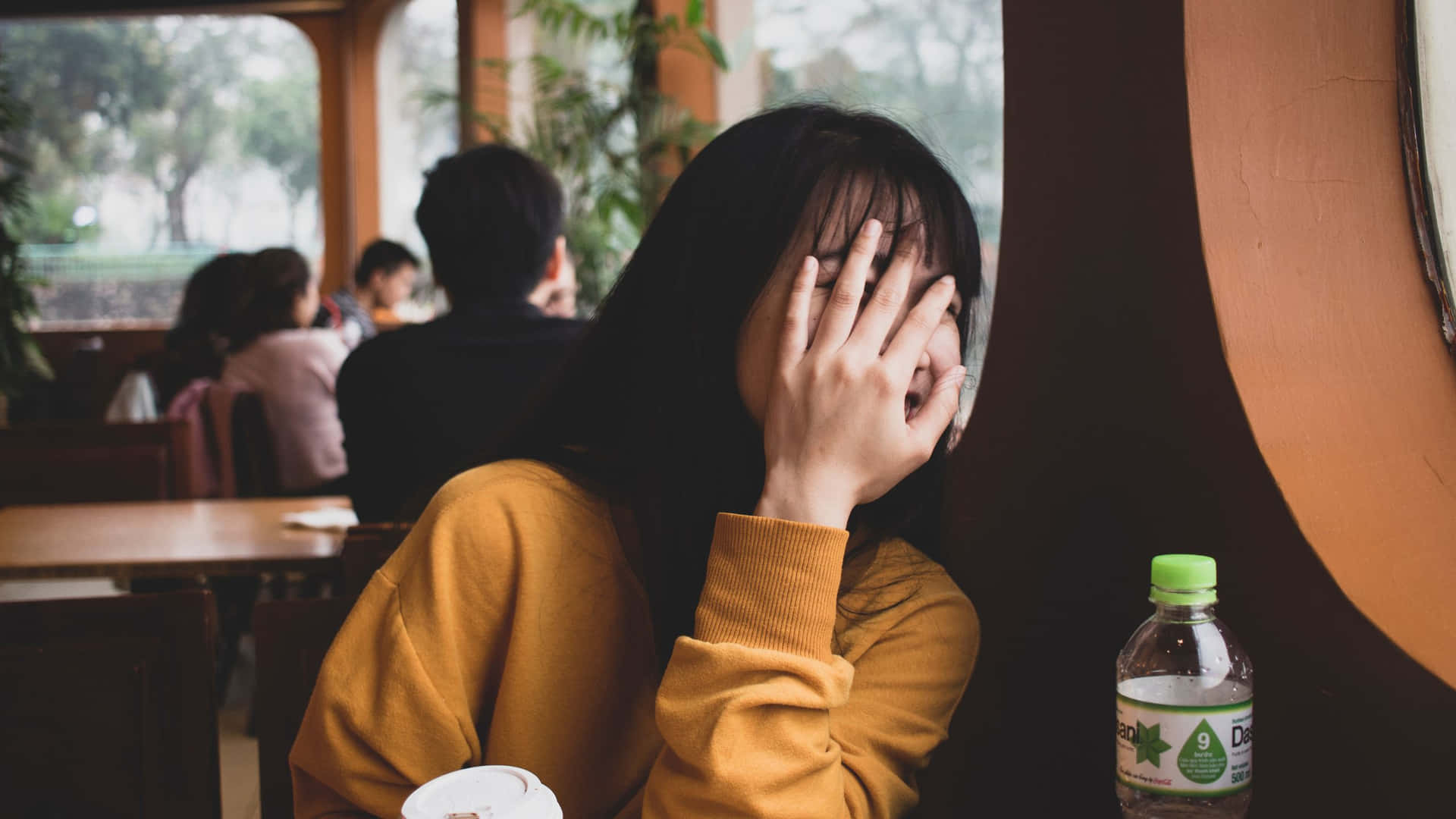 Embarrassed Woman Hiding Facein Cafe.jpg Wallpaper