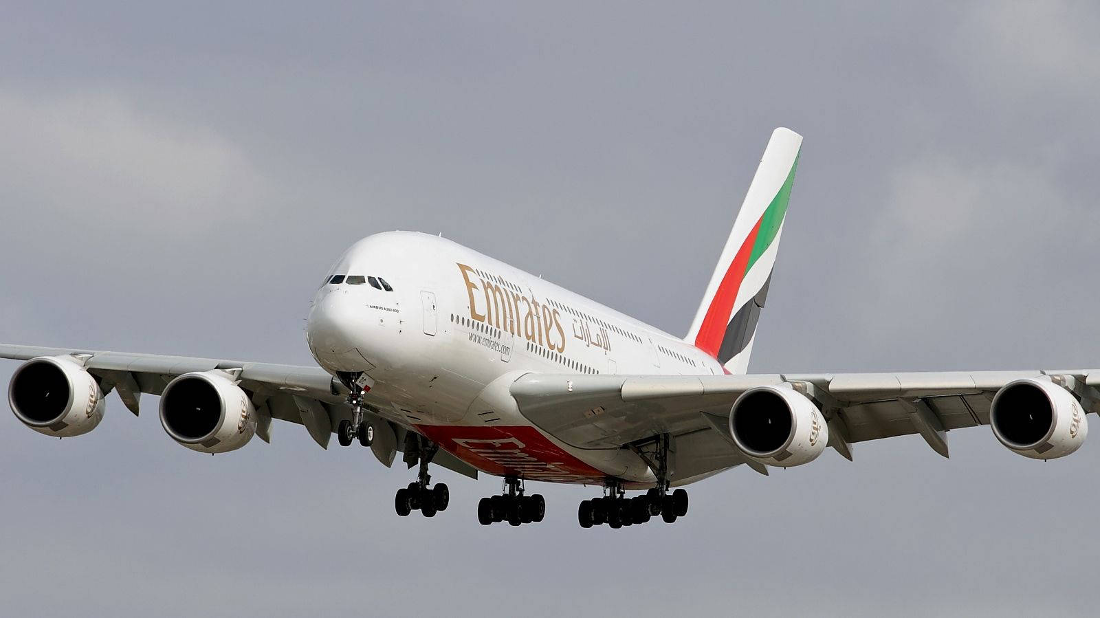 En Emirates Airbus A380 med landingergear, som flyver over byen Wallpaper