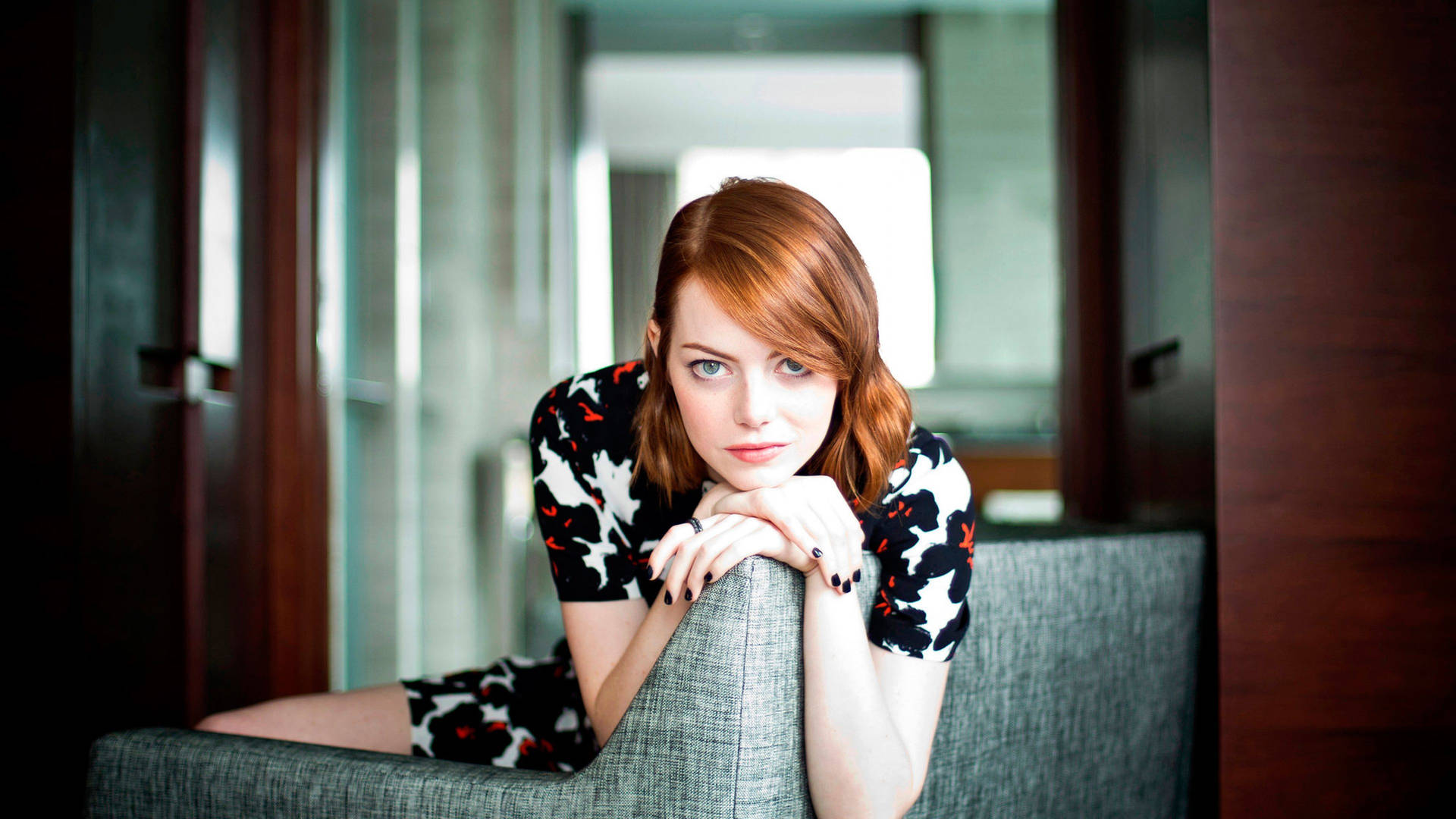 Emma Stone perched on a large couch Wallpaper