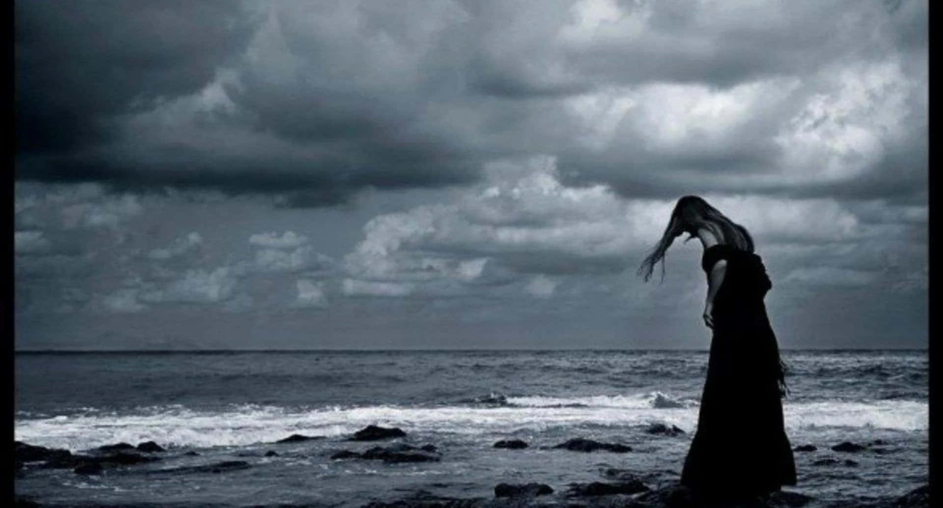 A Woman Standing On The Beach Under A Stormy Sky