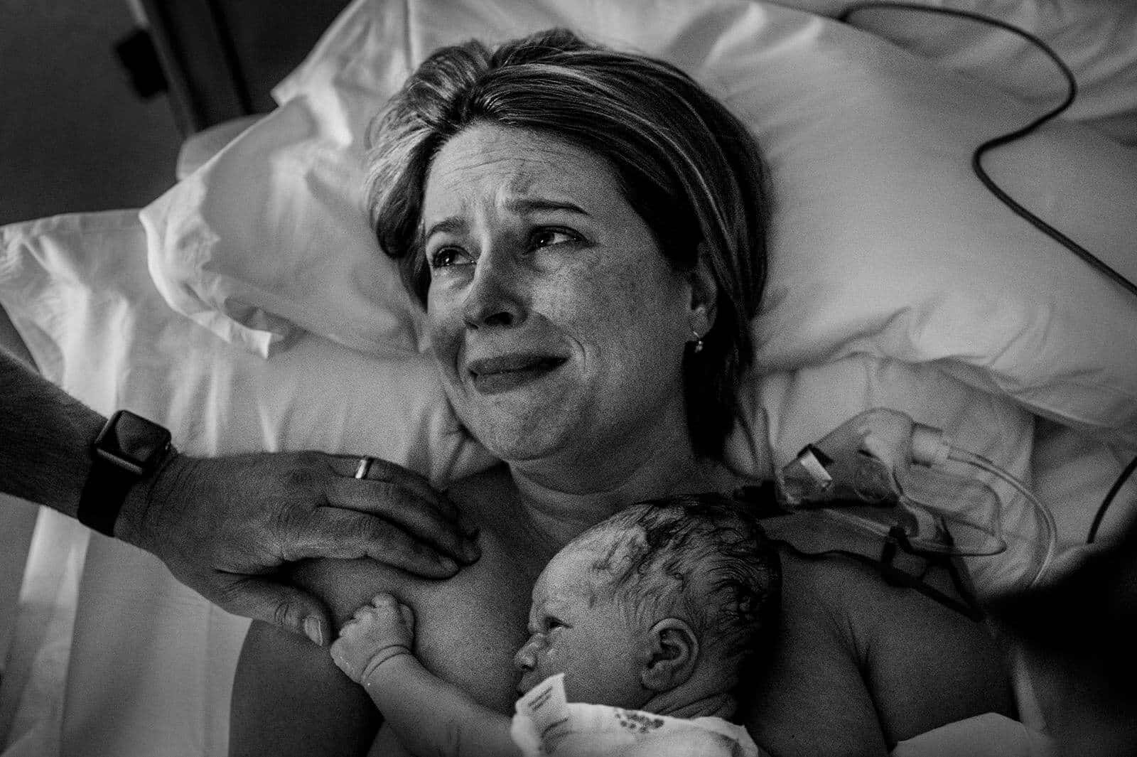 A Woman Is Holding Her Baby In A Hospital Bed