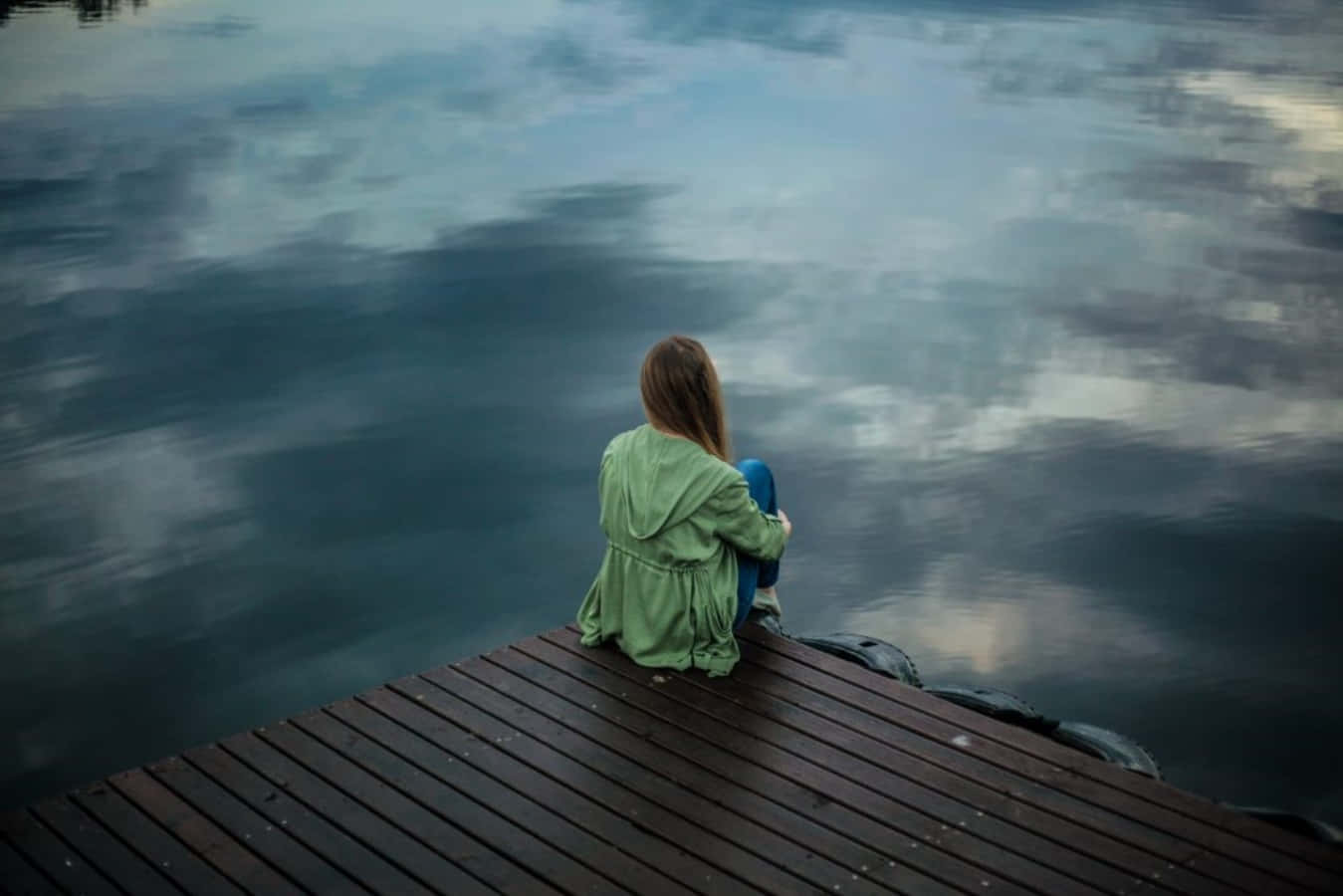 A Girl Sitting On A Dock Looking At The Water