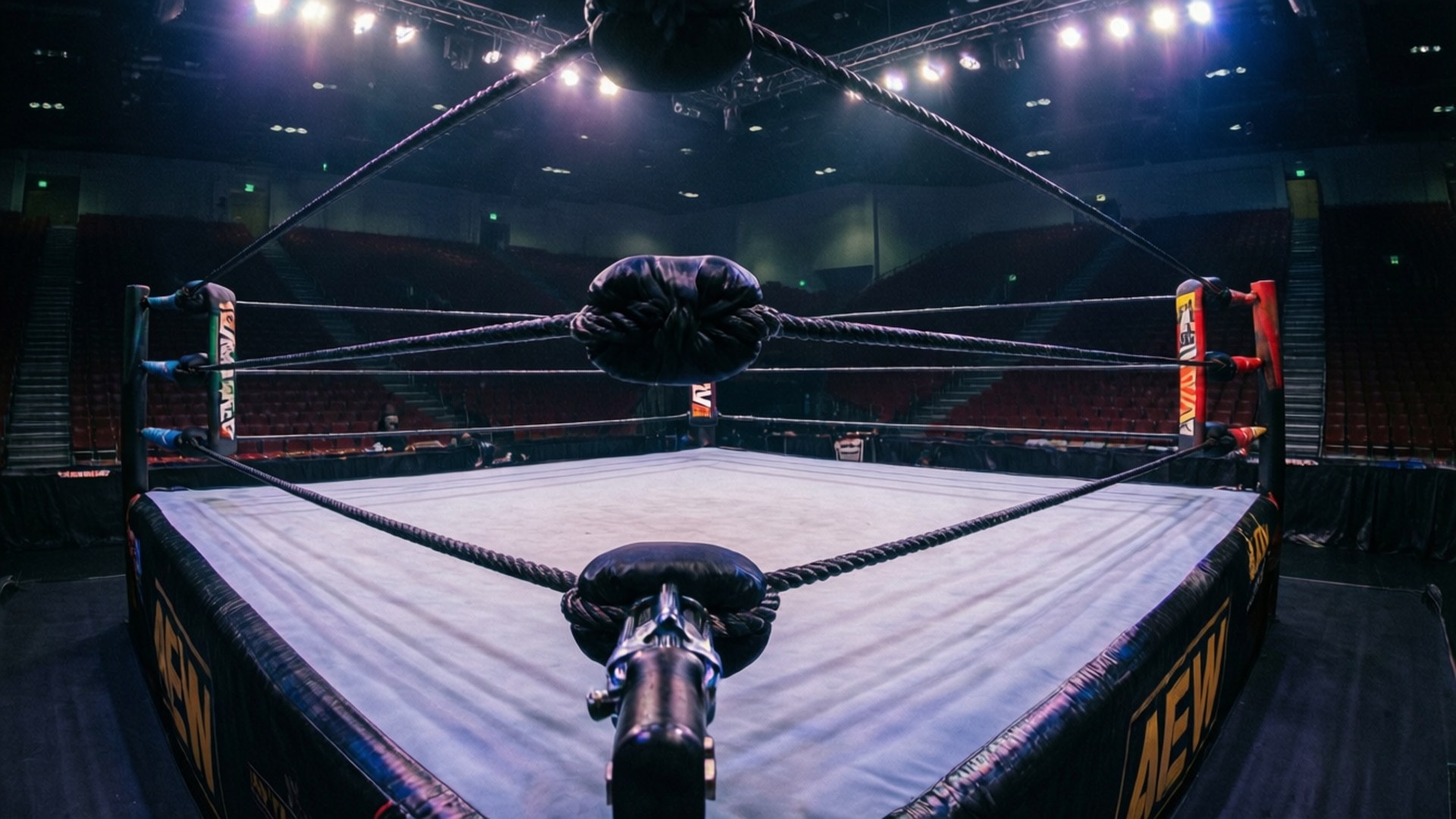 Empty AEW wrestling ring in a moody arena with blue and purple lighting.