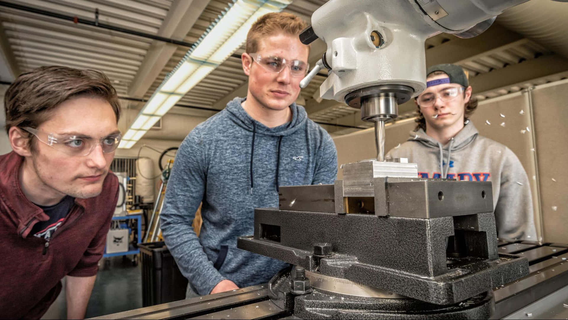 Trestudenter Arbetar På En Maskin I Ett Laboratorium.