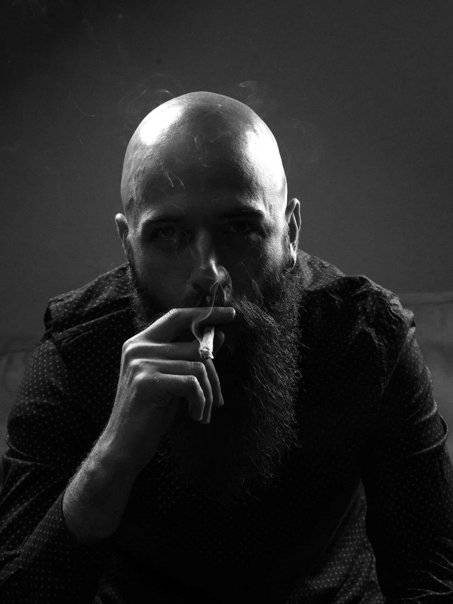 Enigmatic Bald Man Relishing The Pleasure Of Smoking Wallpaper