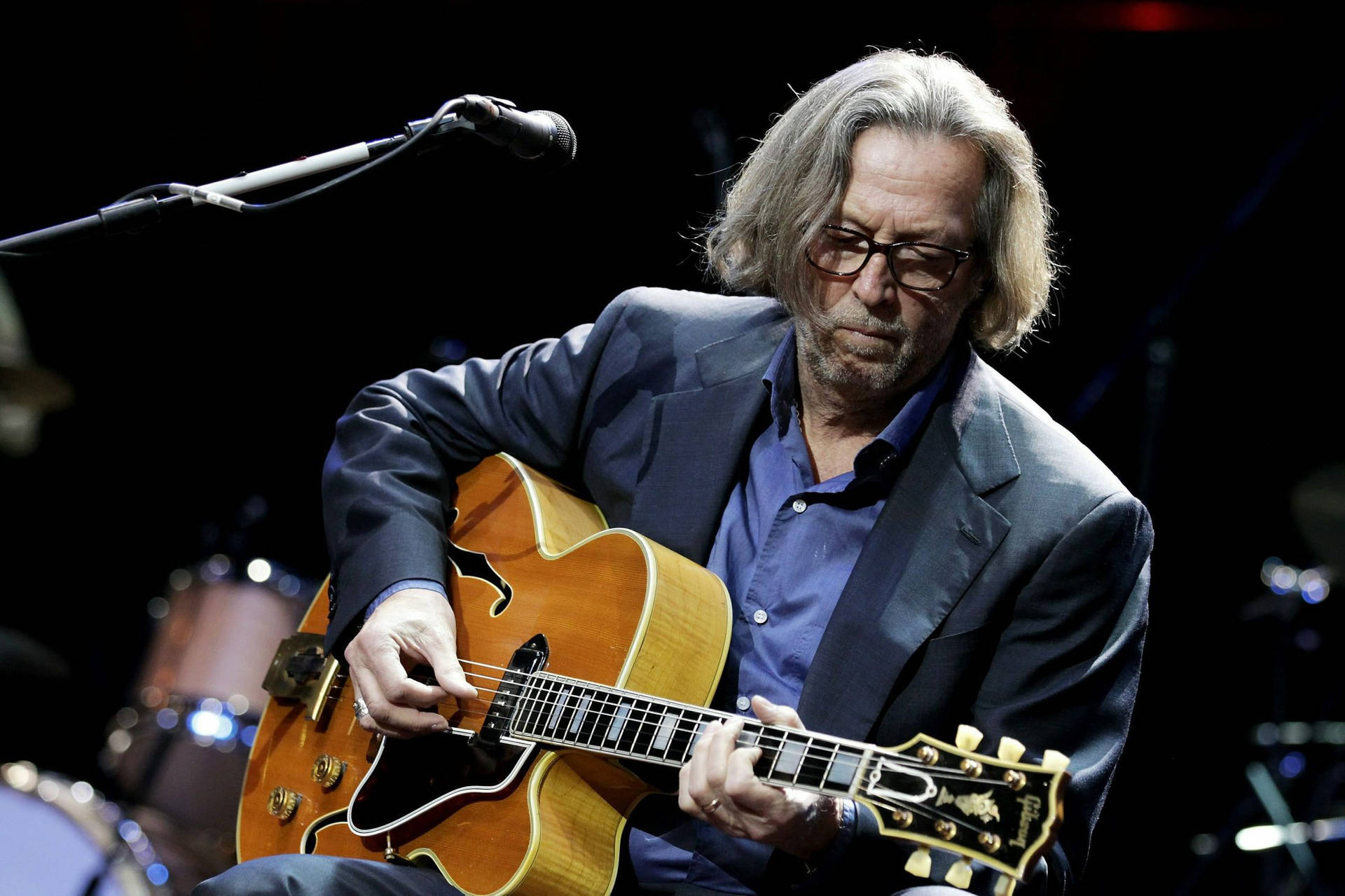 Rock Legend Eric Clapton Engrossed in Playing Acoustic Guitar Wallpaper