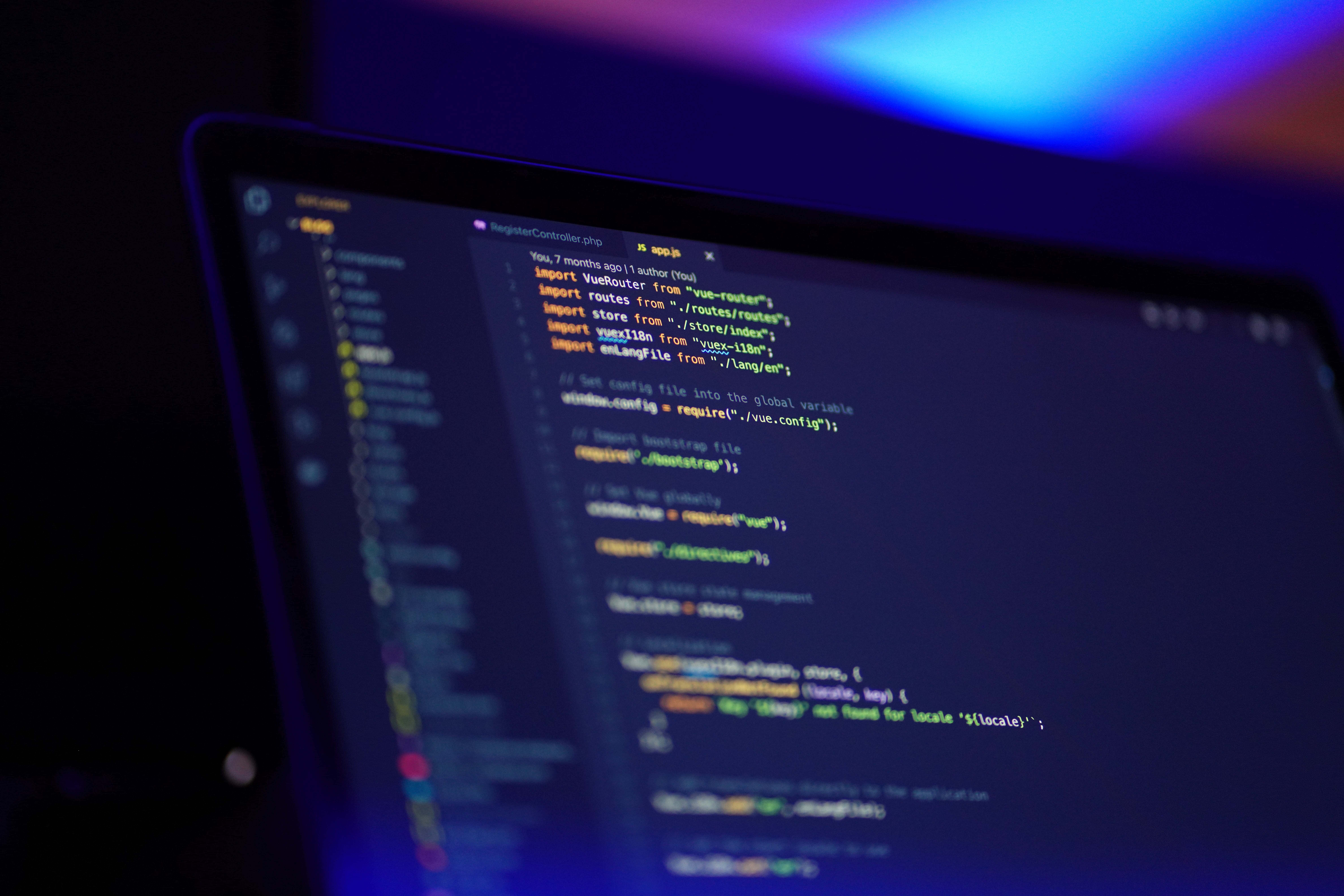 Experienced Programmer Writing Code Background — A close-up of a curved monitor displaying colorful code in a dark theme, bathed in ambient blue and purple light.