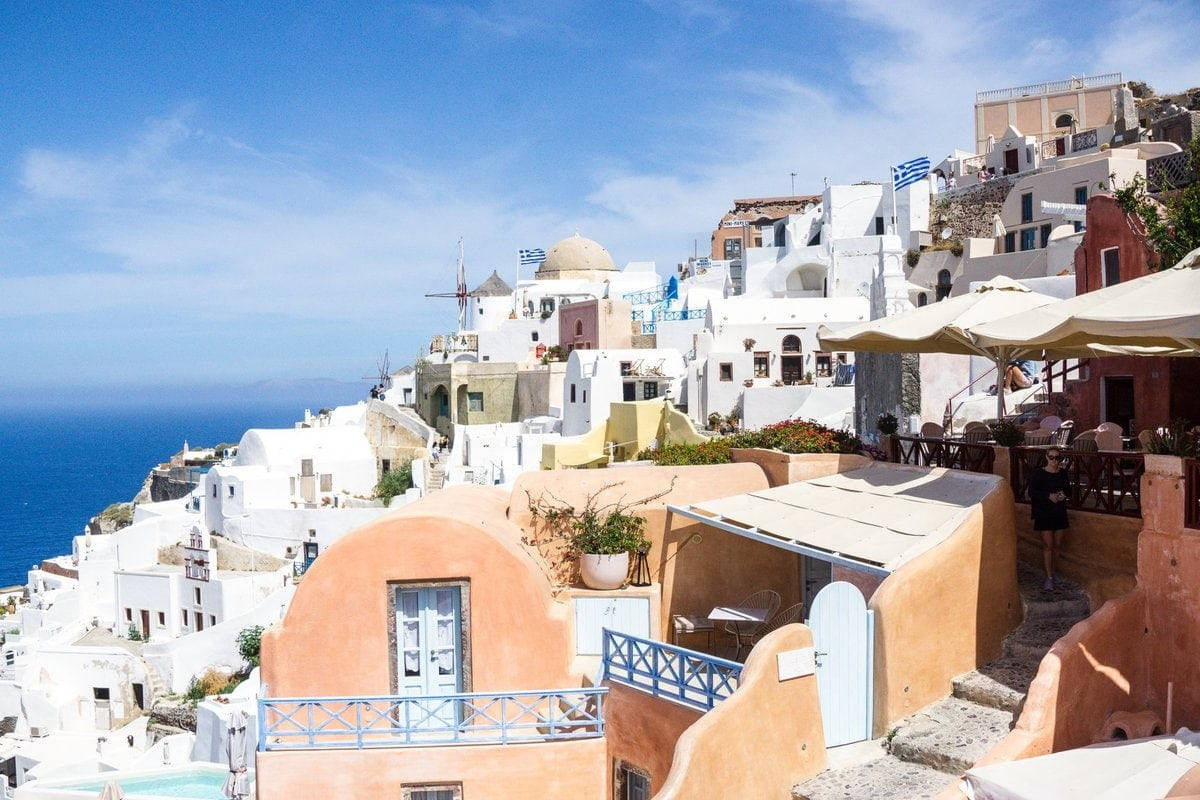 An exquisite view of Santorini's iconic blue-domed churches and whitewashed houses overlooking the shimmering Aegean Sea. Wallpaper