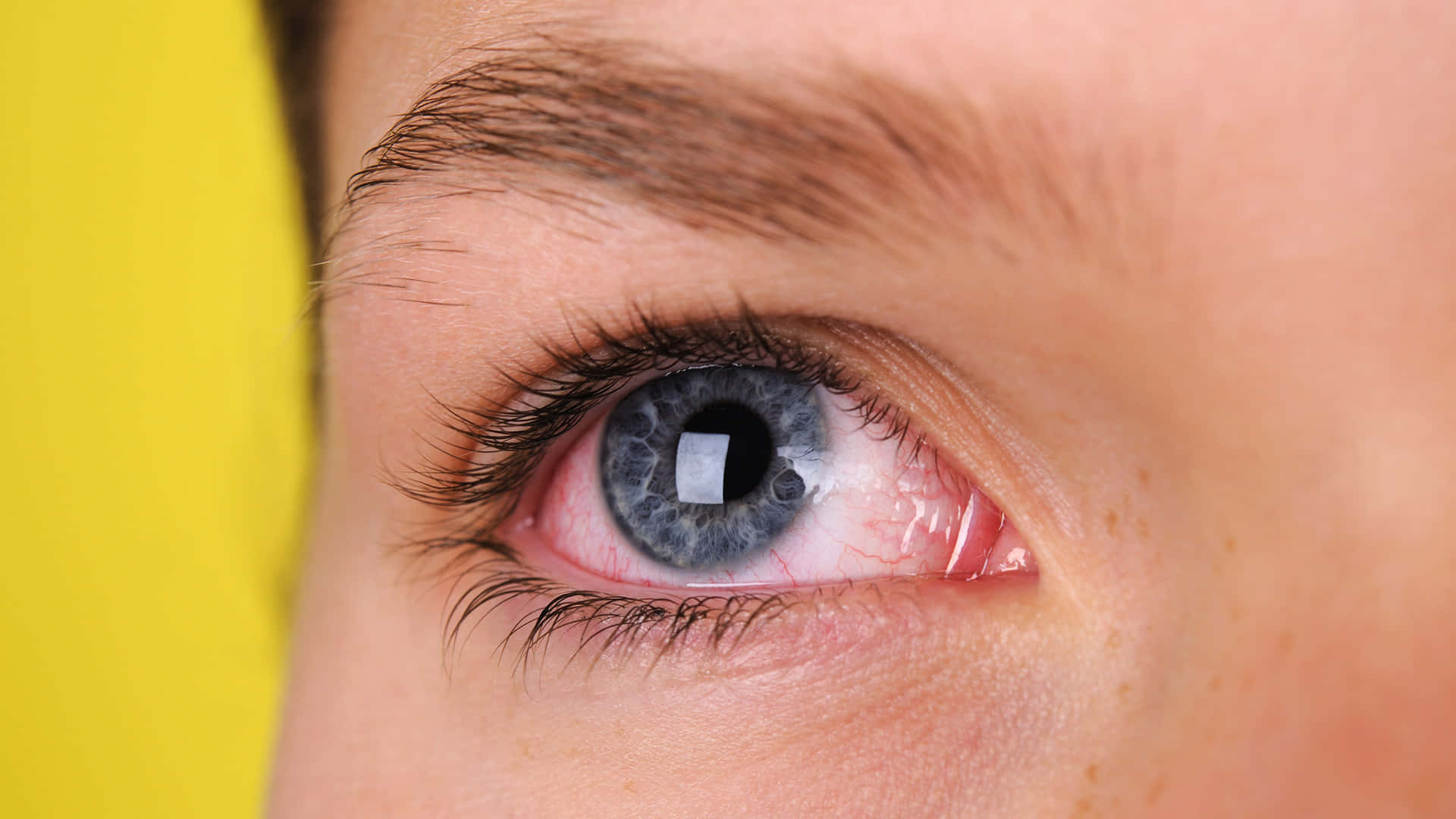 A Woman's Eye With Blue Eyes And A Yellow Background