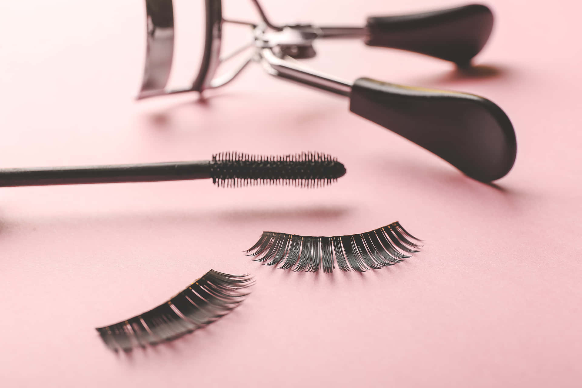 A Pair Of Eyelash Curlers And Mascara On A Pink Background