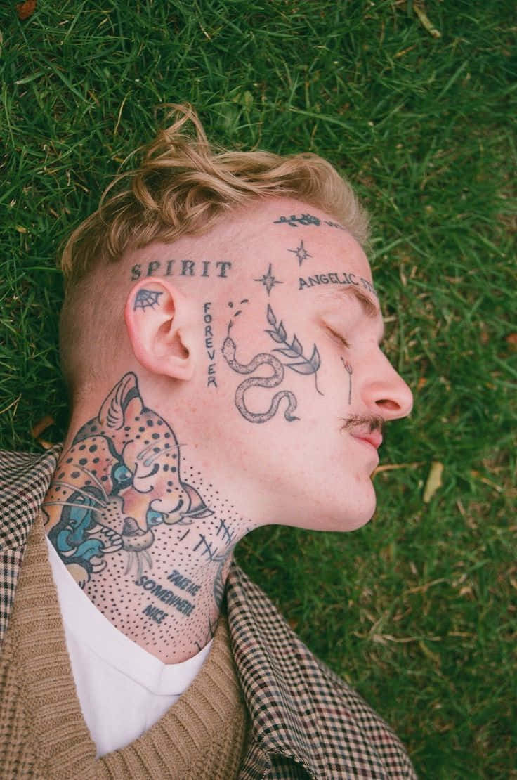A Man With Tattoos On His Face Laying On The Grass