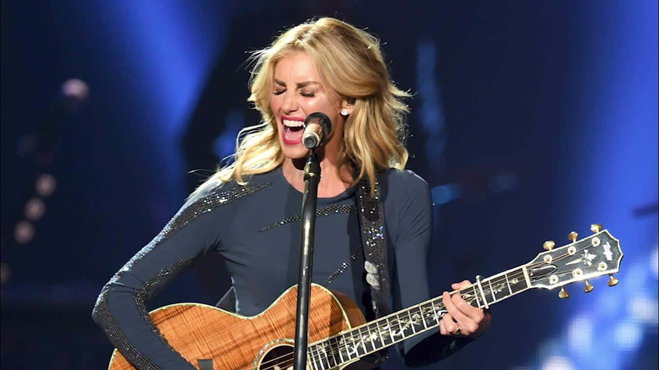 A Woman Singing Into A Microphone While Holding An Acoustic Guitar