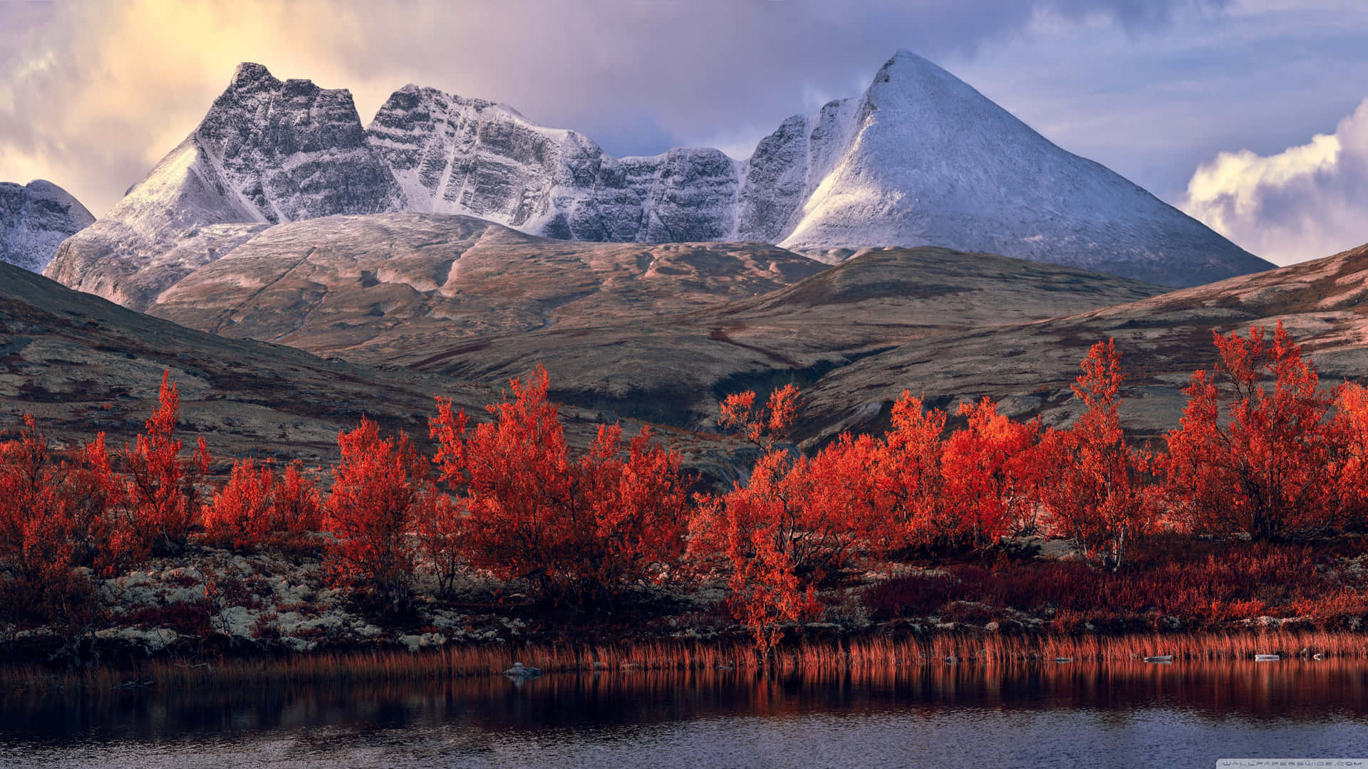 Et bjergkæde med røde træer og en sø ved foden af det. Wallpaper