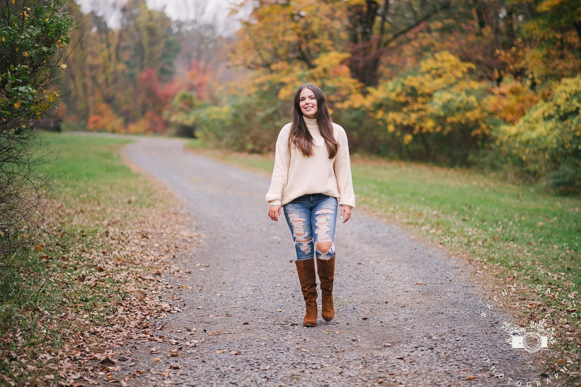 A Girl In A Sweater And Boots Walking Down A Dirt Road