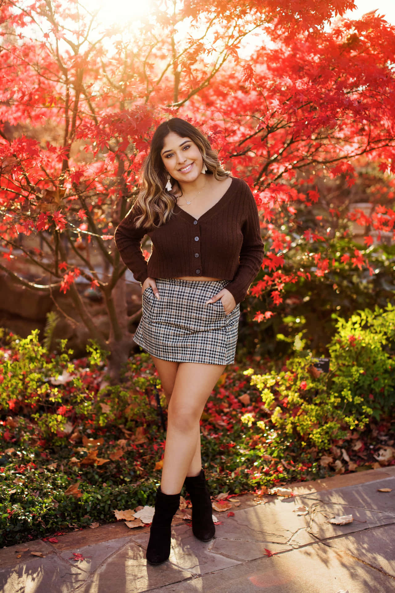 A Woman In A Plaid Skirt Poses In Front Of A Red Tree