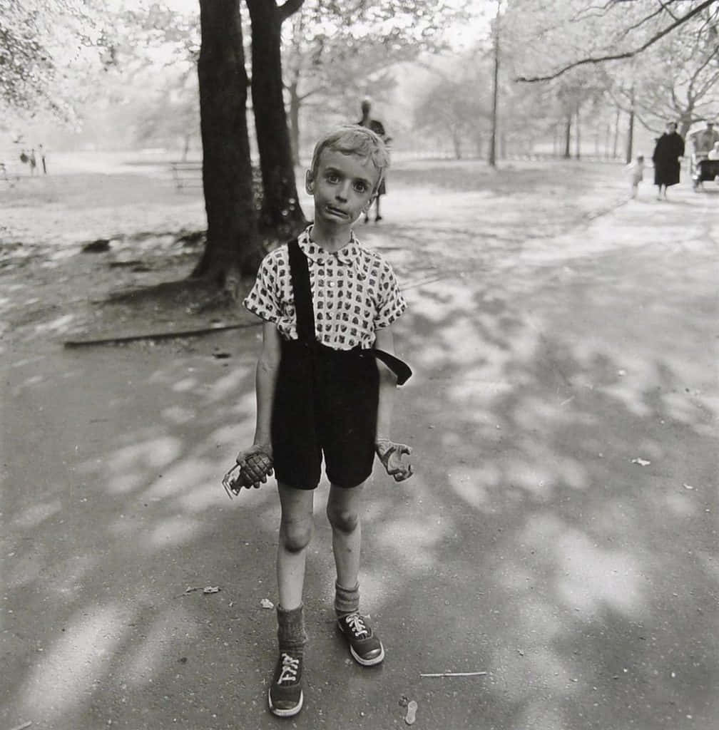 A Boy In Overalls Standing In A Park