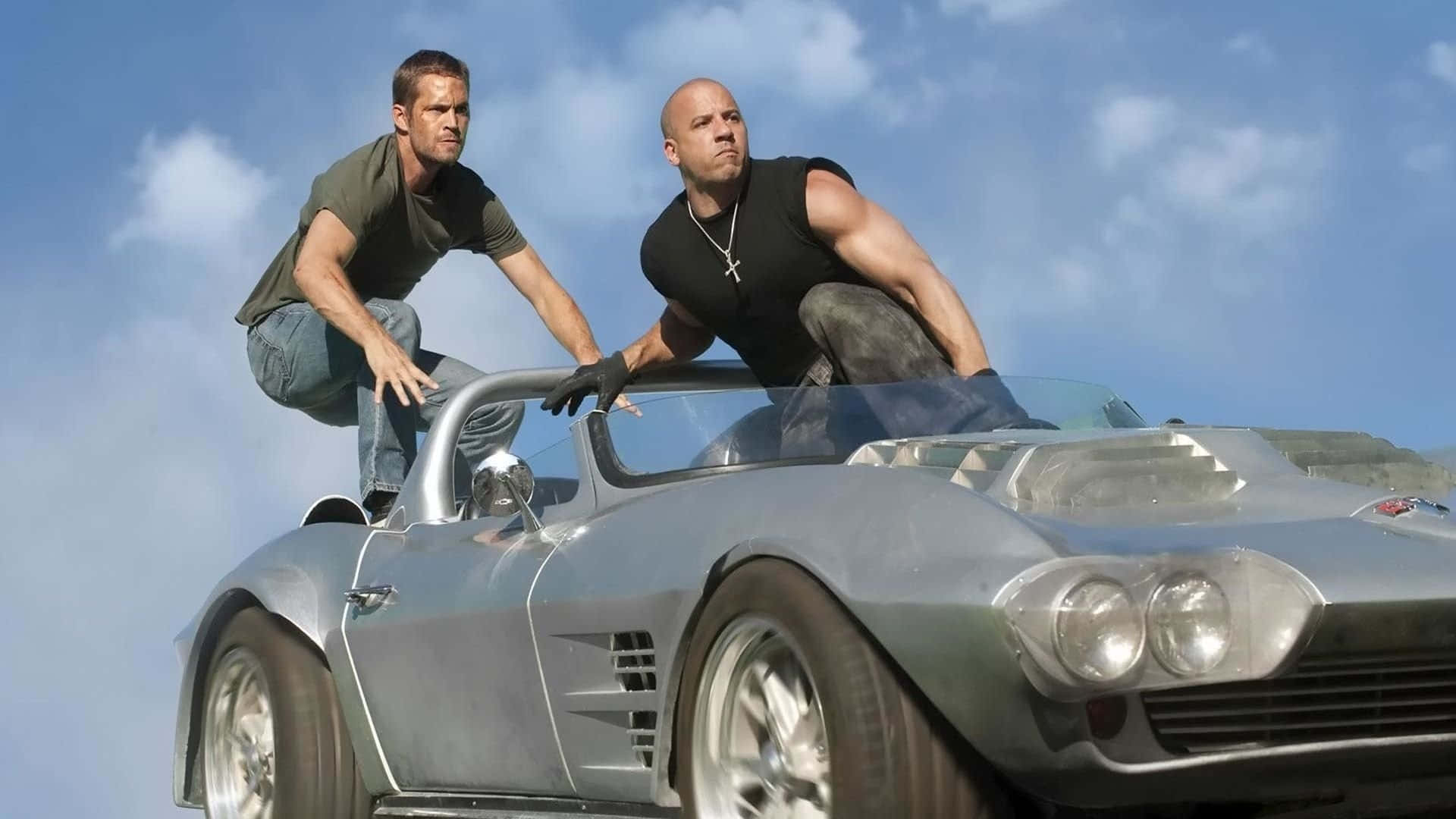 Two Men Are Standing On Top Of A Silver Car Wallpaper
