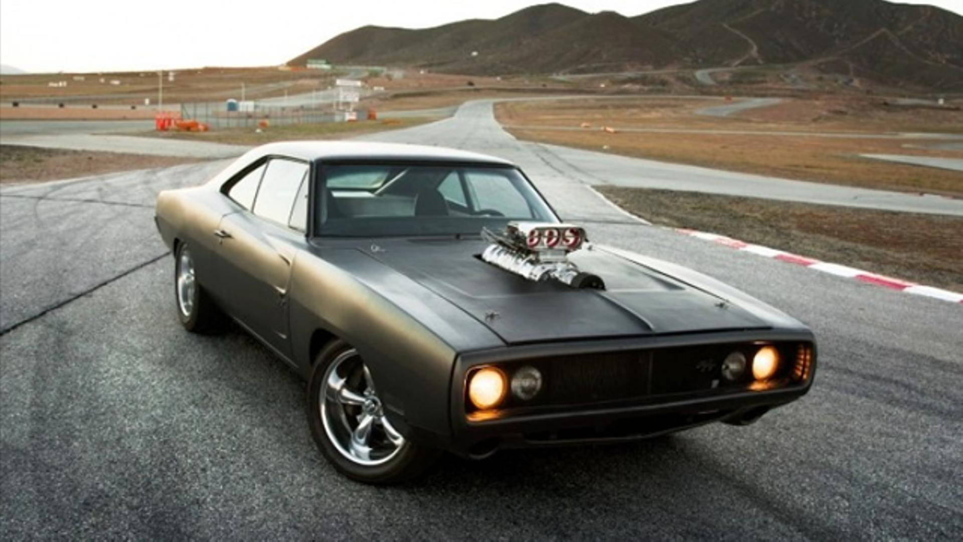 A Black Muscle Car Is Driving Down A Road Wallpaper
