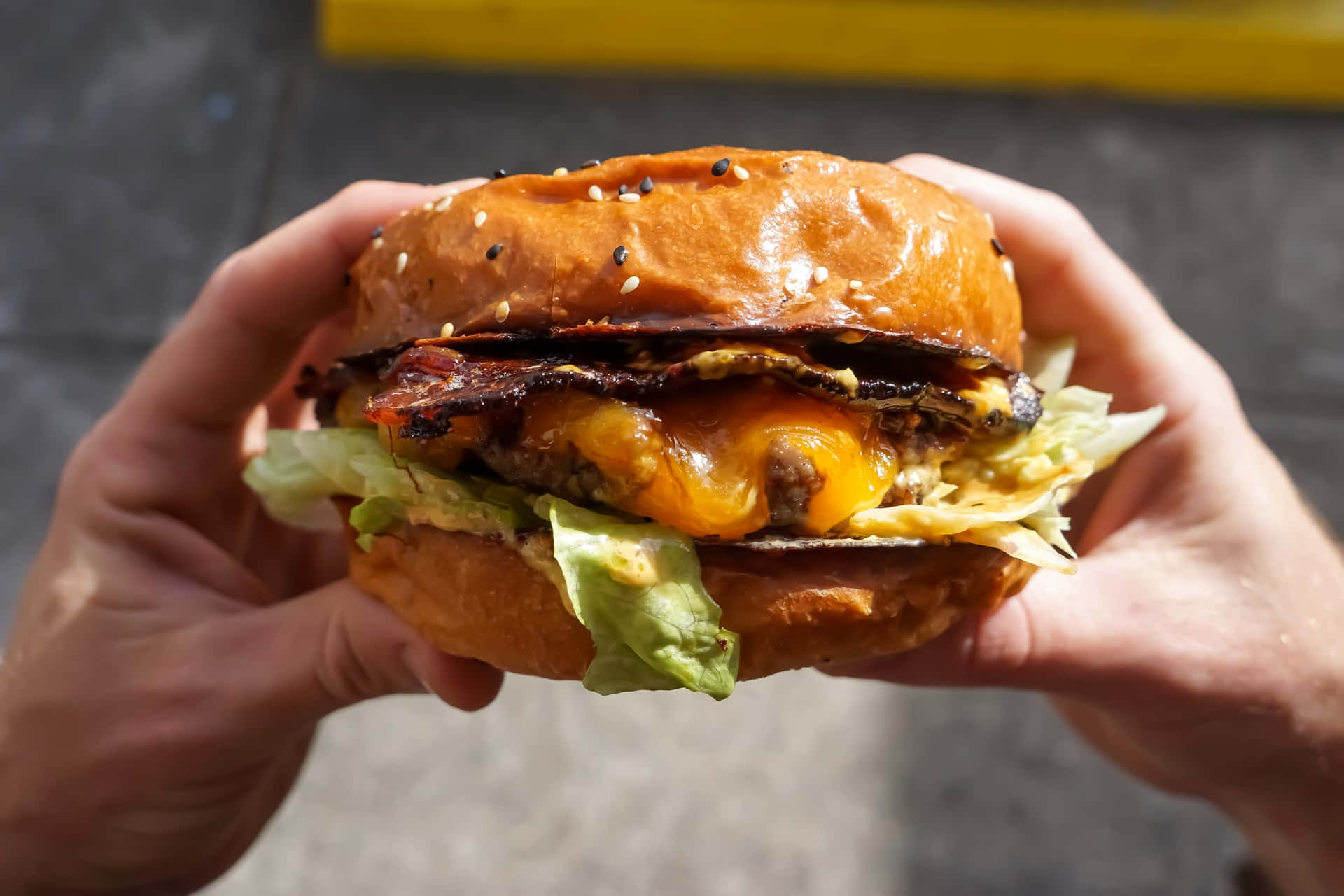 A Person Holding Up A Burger With Bacon And Cheese