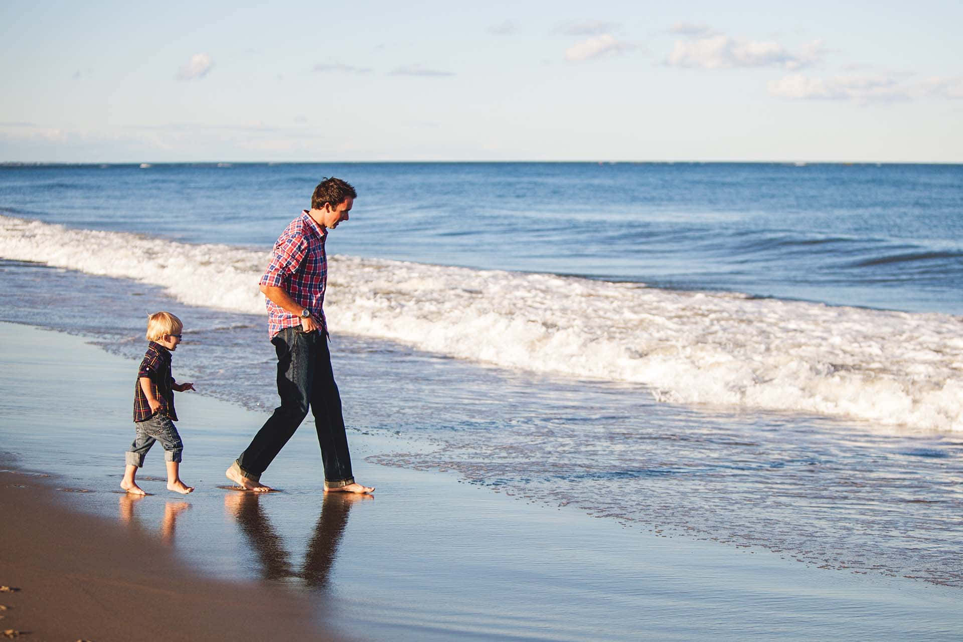 Fader og mandligt barn går barfodet på stranden Wallpaper