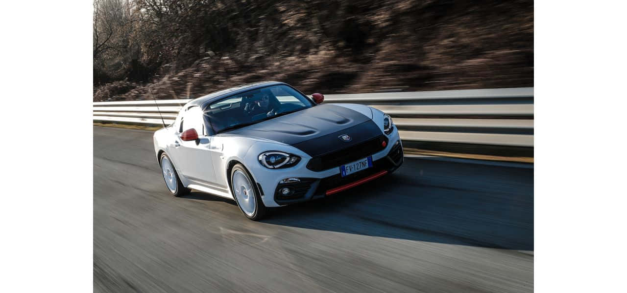 Fiat 124 Spider cruising on a scenic road Wallpaper