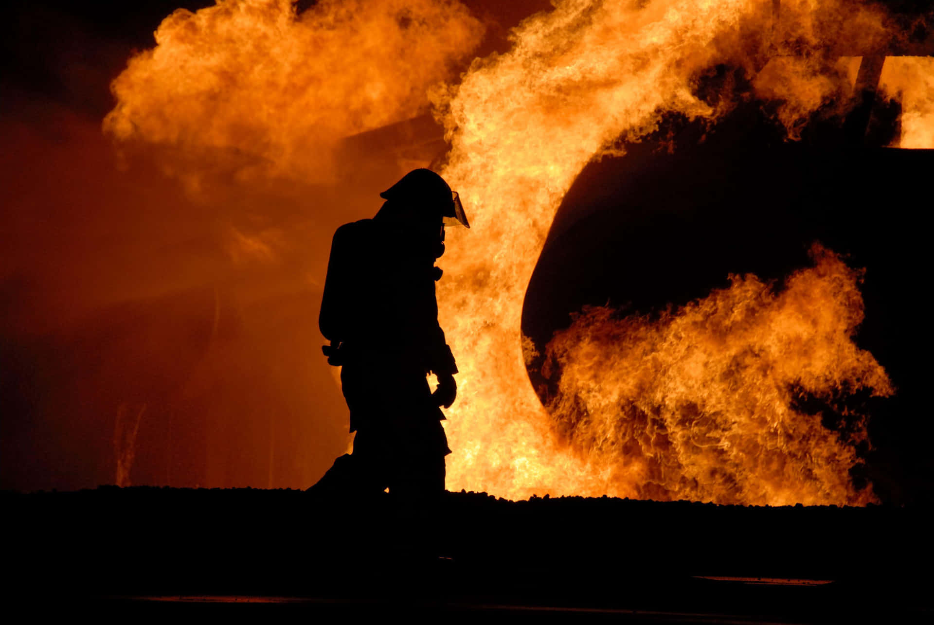 A Firefighter Walks Past A Large Fire