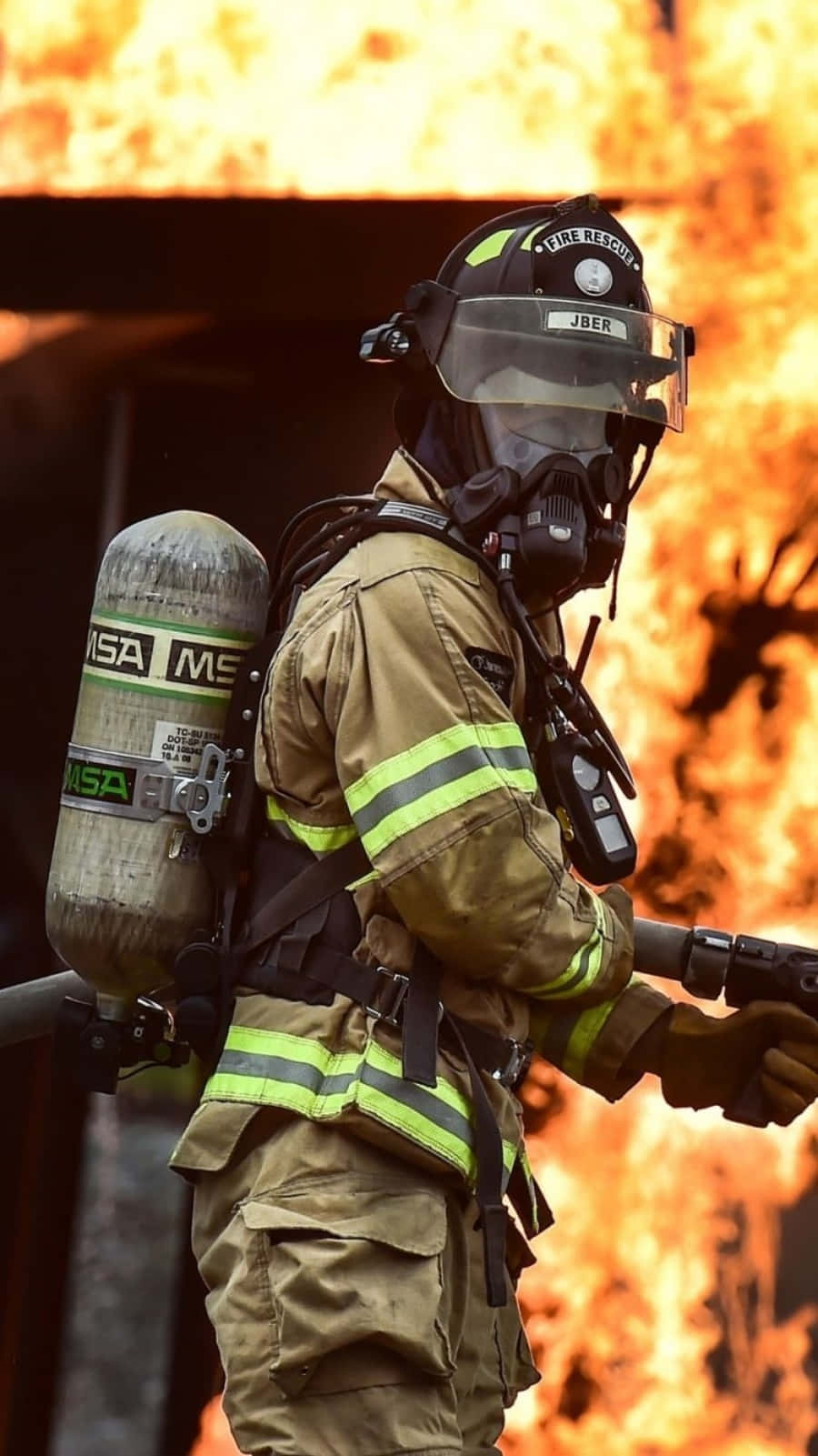 En brandmand holder en slange foran en brandbil Wallpaper