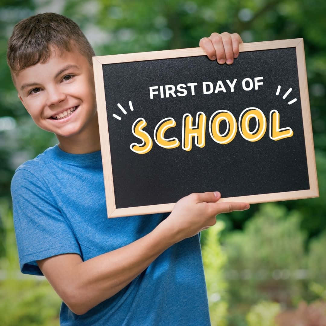 A Boy Holding Up A Chalkboard That Says First Day Of School