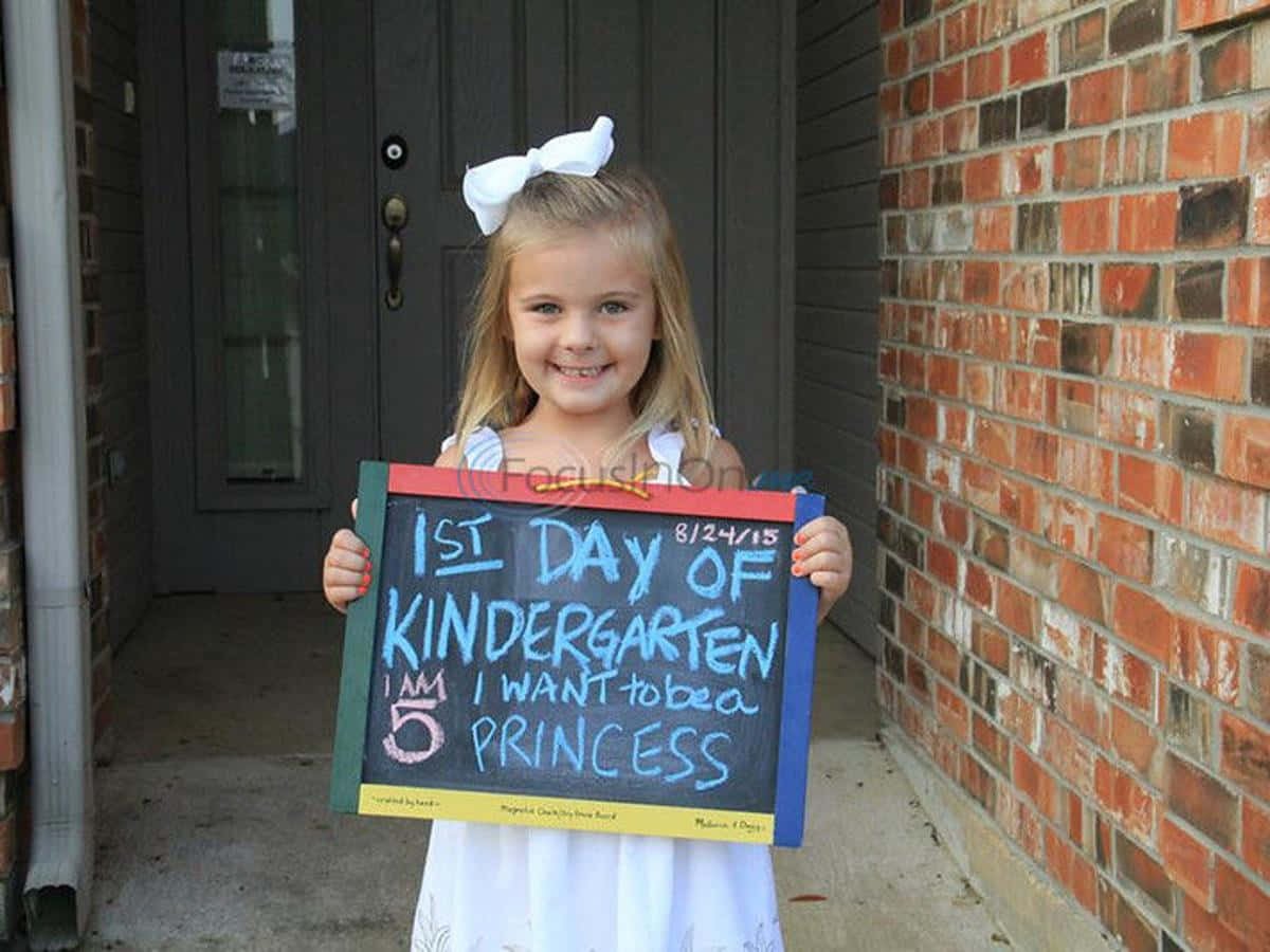 A Little Girl Holding Up A Chalkboard Sign That Says First Day Of Kindergarten