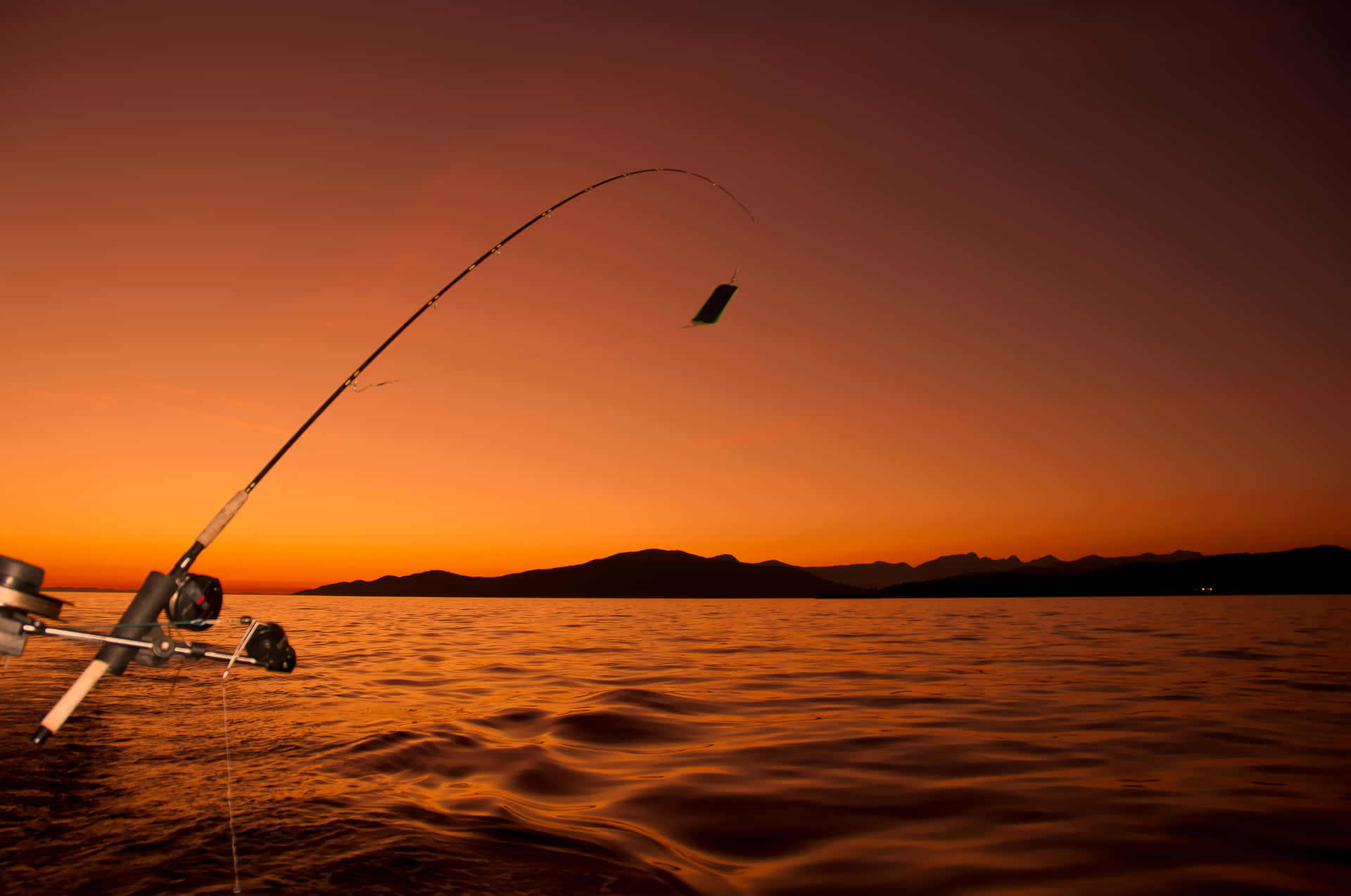 Angler in action holding a fishing rod by a beautiful lakeside Wallpaper