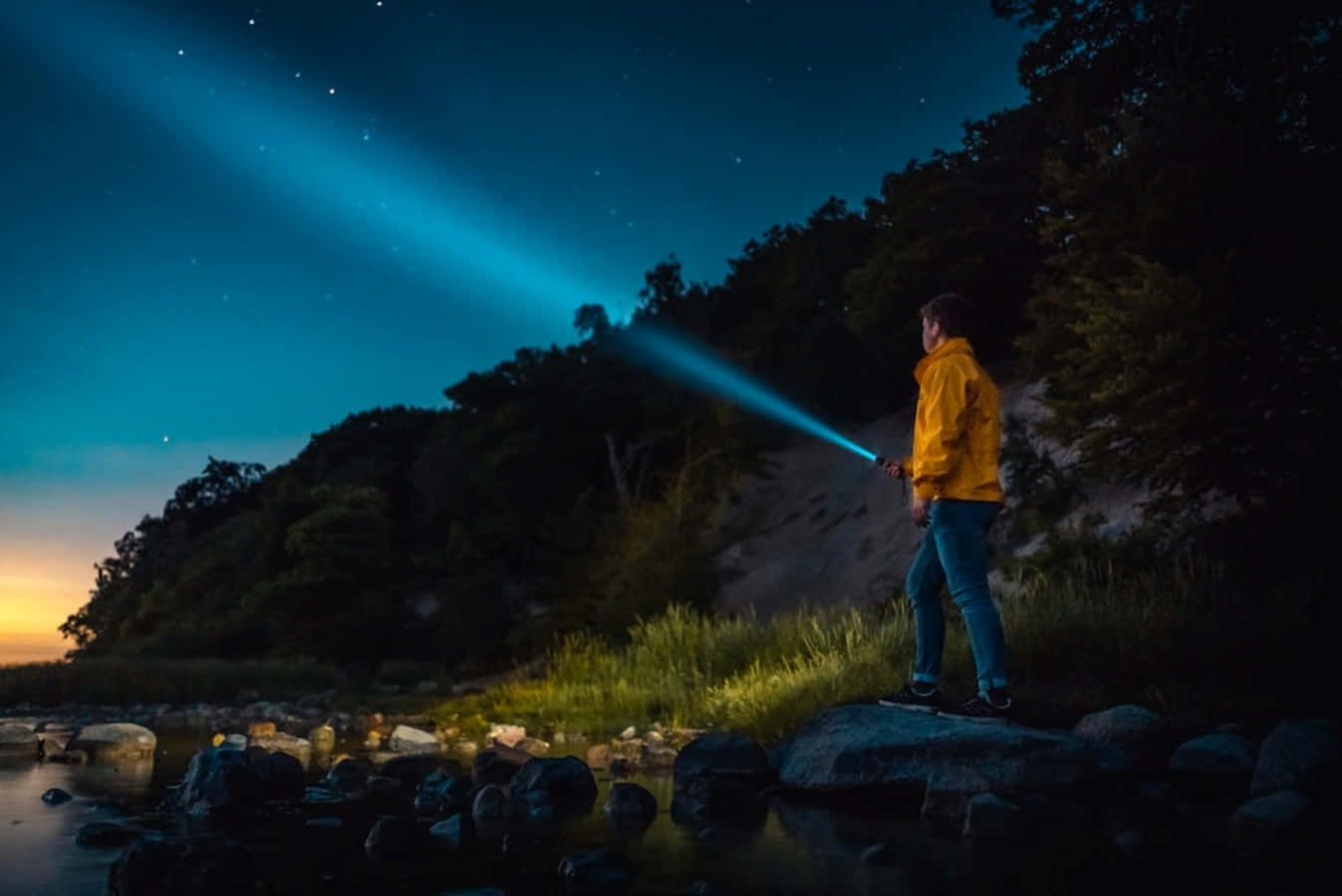 A Man Standing On Rocks At Night With A Flashlight