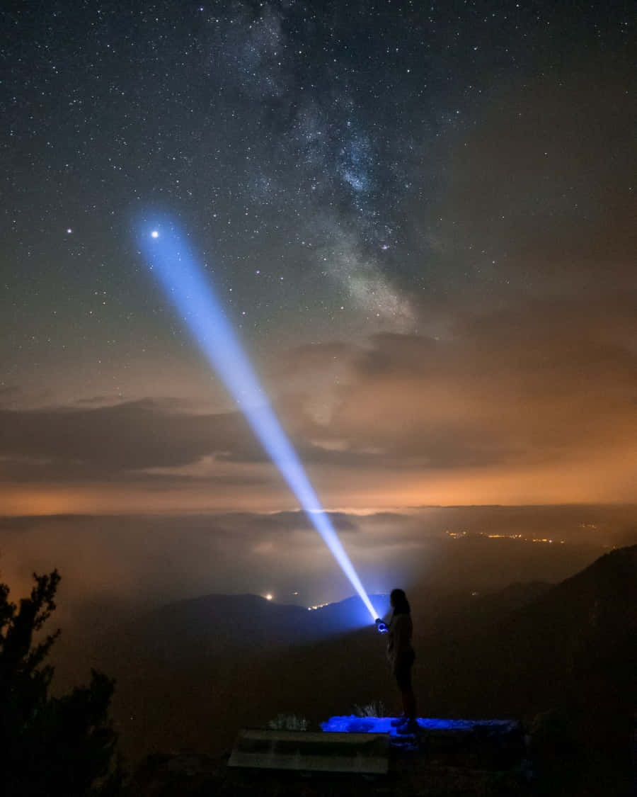 A Person Standing On A Mountain Top With A Flashlight