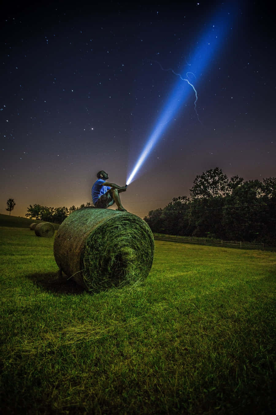 A Man Is Sitting On A Hay Bale With A Flashlight