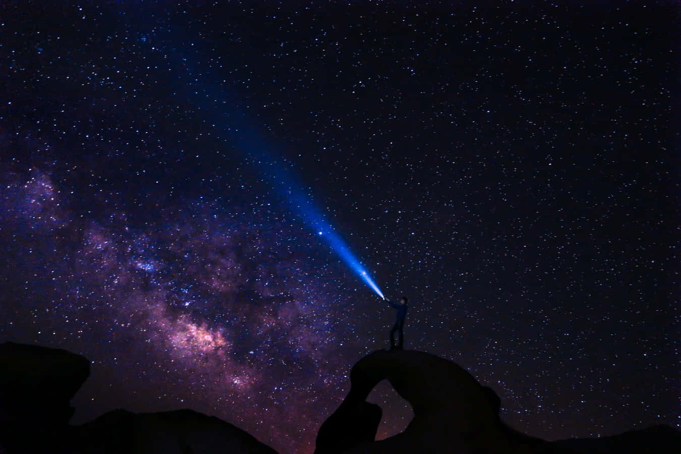 A Person Standing On A Rock With A Flashlight Under The Milky Way