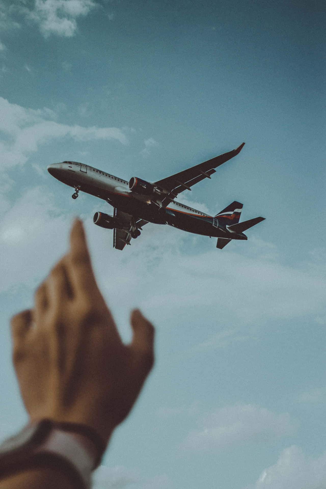 En persons hånd rækker ud mod et fly, der flyver over et blåt felt. Wallpaper