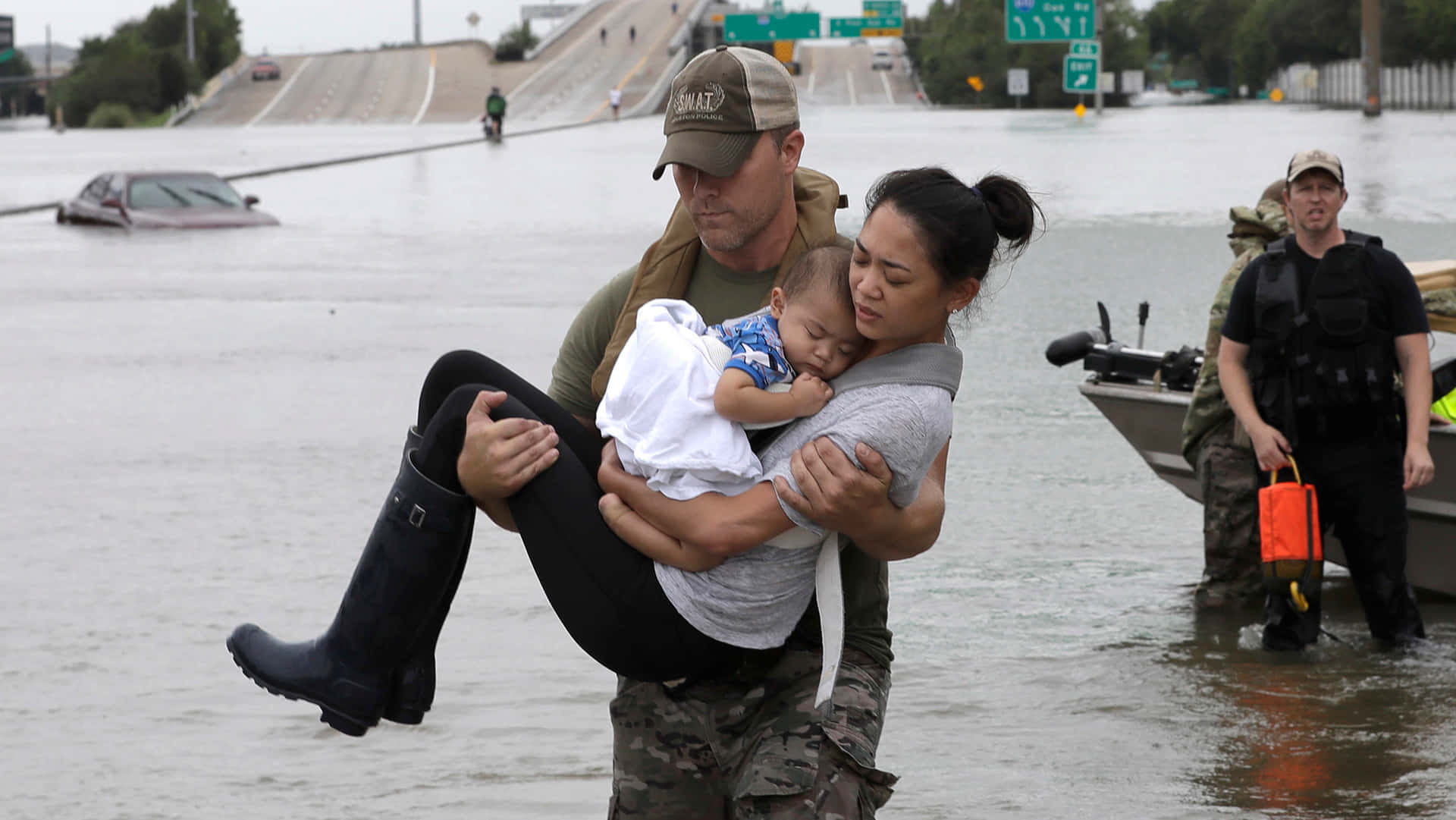 A Man Is Carrying A Child Through A Flooded Street