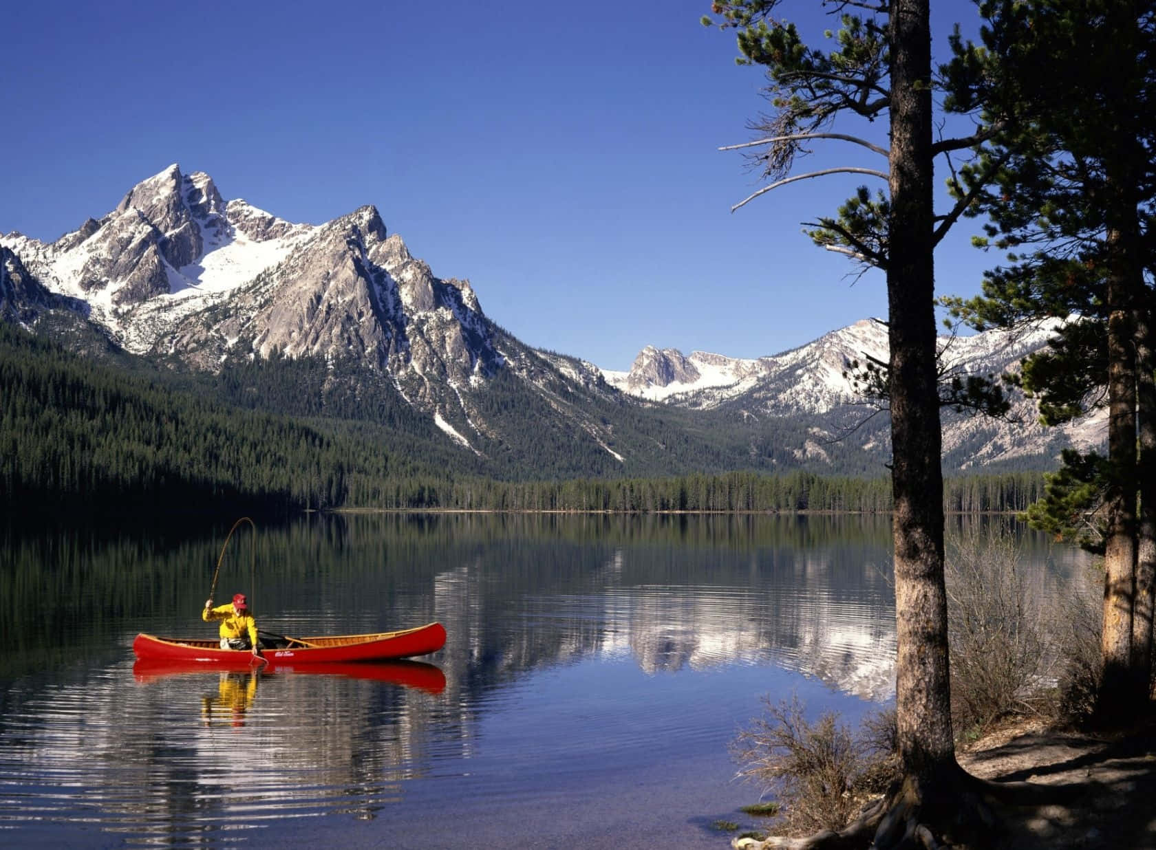 En mand padler en rød kano på en sø med bjerge i baggrunden. Wallpaper