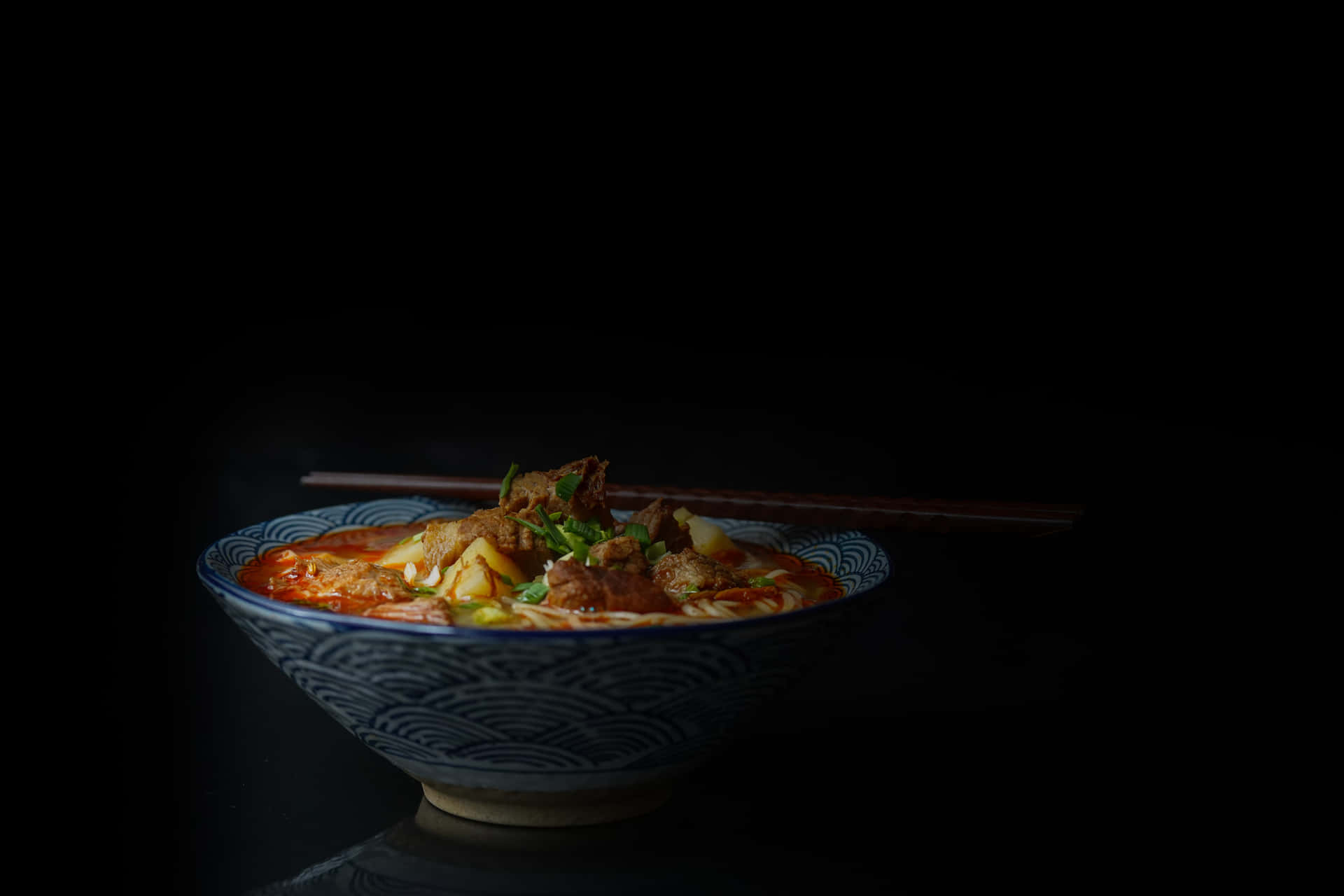 a bowl of soup with chopsticks on a black background