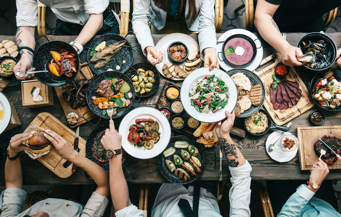 En gruppe mennesker, der spiser mad ved et bord. Wallpaper