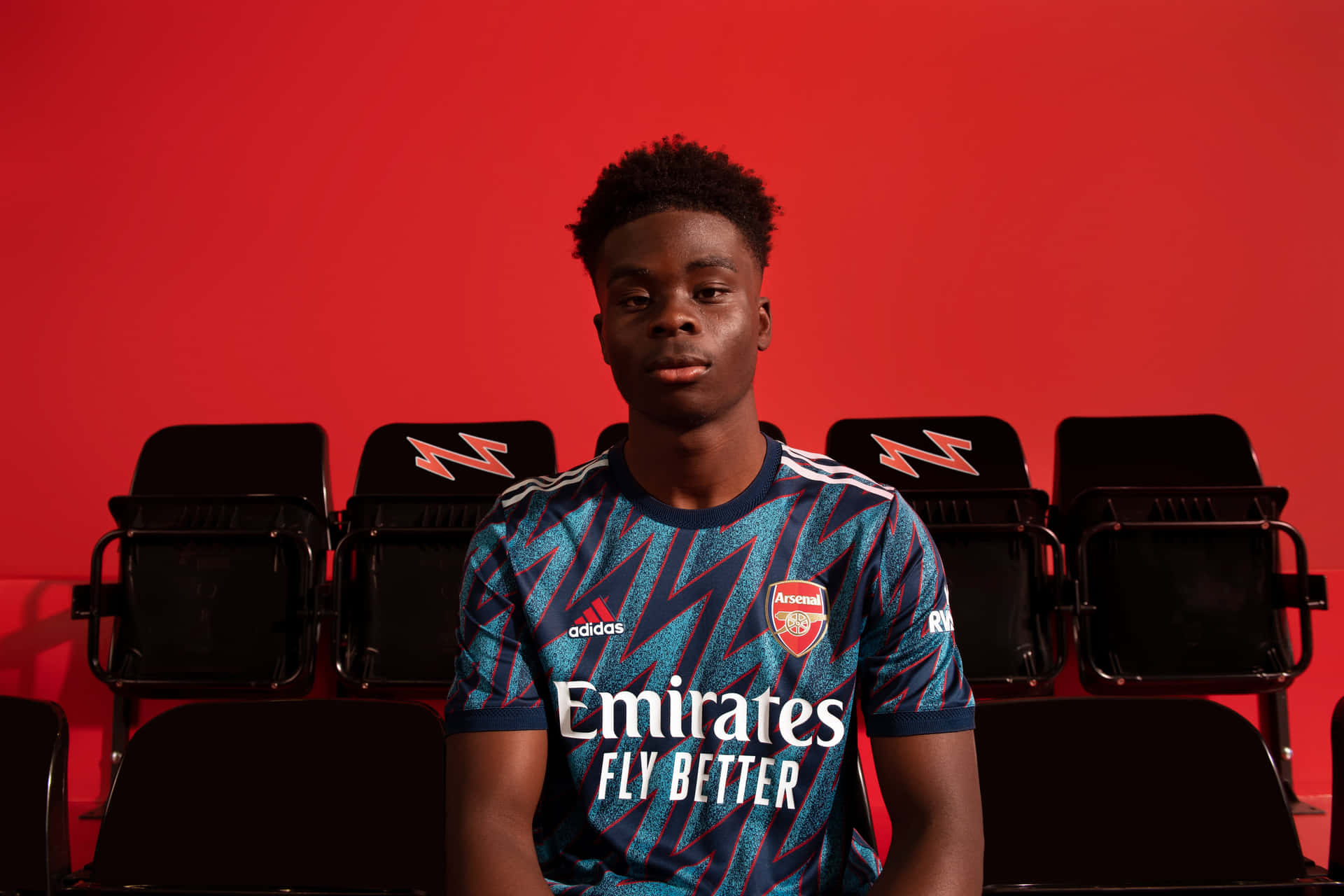 Footballerin Arsenal Kit Seated Against Red Background Wallpaper