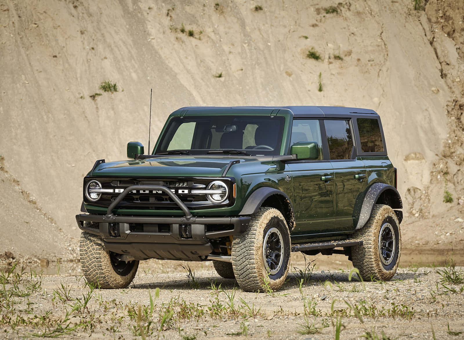 The Green Ford Bronco Is Parked In A Dirt Field