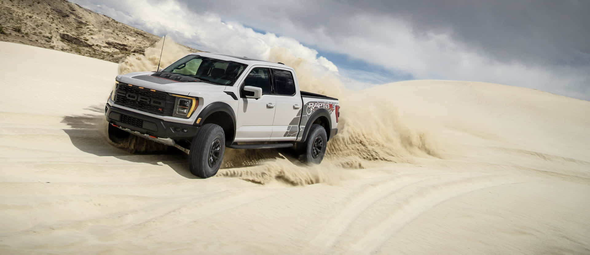 The White Ford F - 150 Raptor Is Driving Through The Sand Dunes Wallpaper