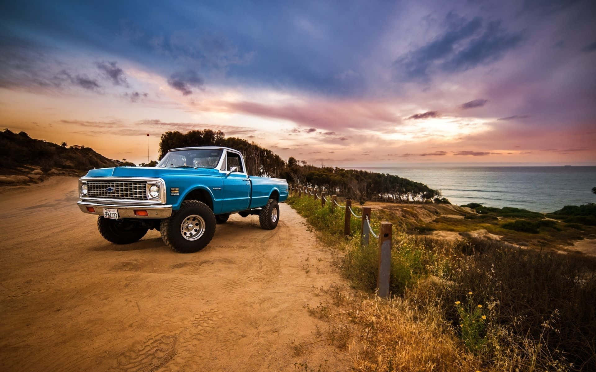 A Blue Truck Is Parked On A Dirt Road Near The Ocean Wallpaper